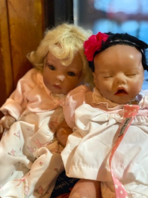 Two realistic-looking baby dolls dressed in pink and white outfits sitting side by side.