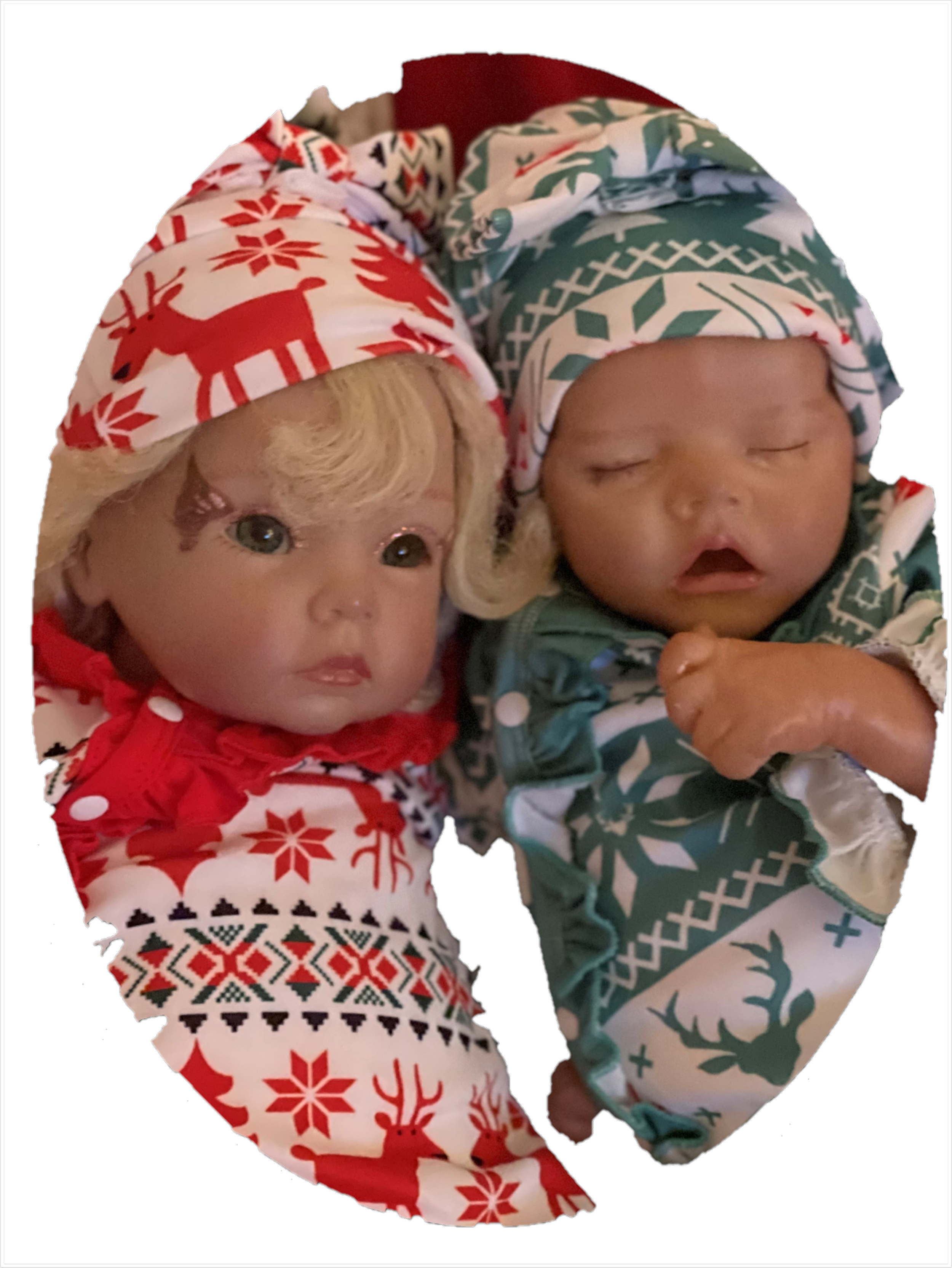 Two realistic baby dolls dressed in holiday-themed pajamas and hats, lying together on a surface with a black background.