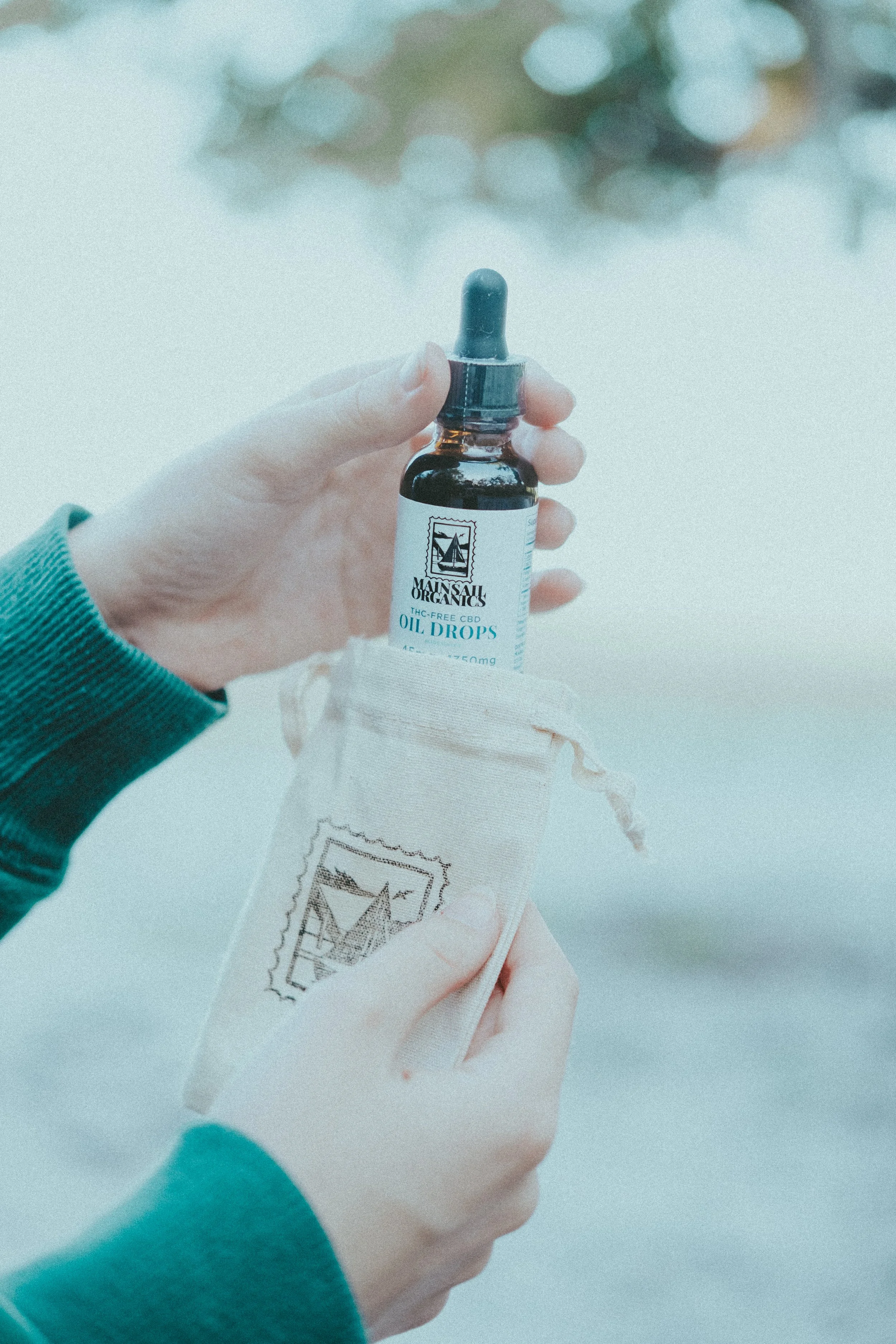 Person holding a small bottle of THC-free CBD oil drops next to a cloth bag.