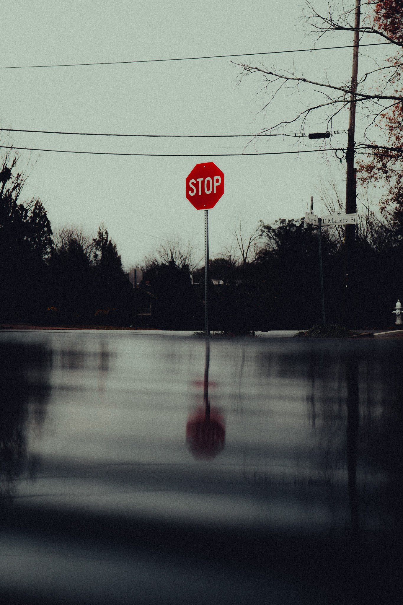 A red stop sign on a street with a street sign that reads E Marietta St in the background. The image is taken from a low angle, possibly from the hood of a car, reflecting the stop sign on the surface.