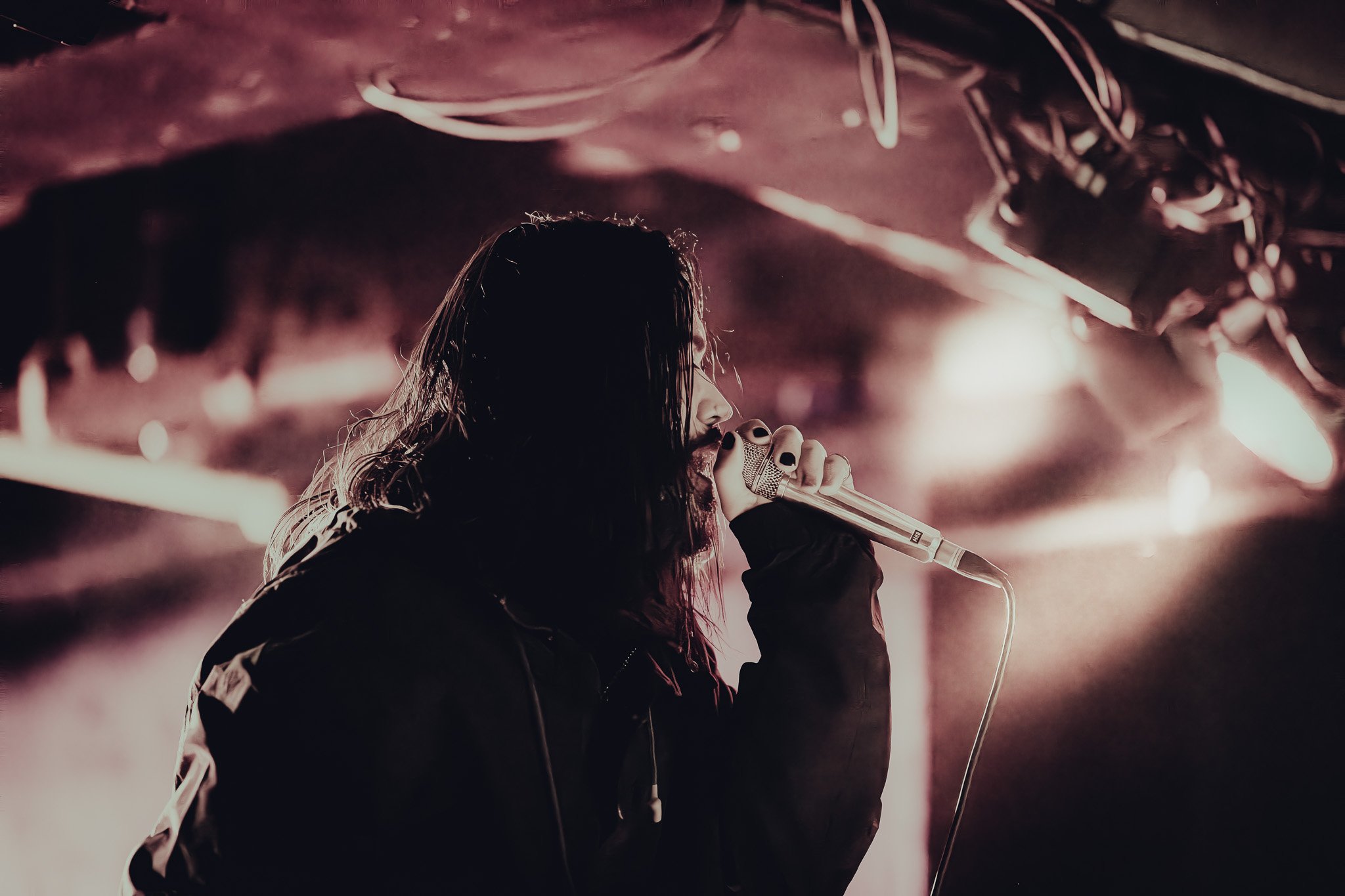 A person singing into a microphone on stage with dramatic lighting and a dark background.