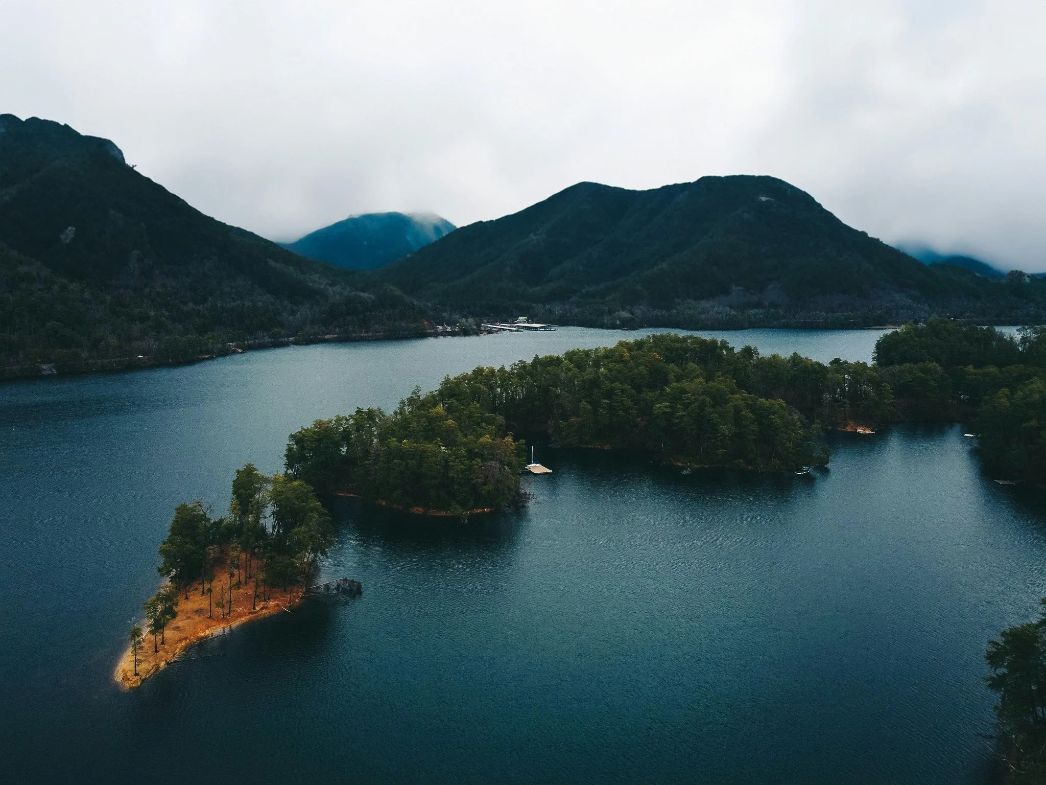 A scenic view of a lake surrounded by lush green islands and mountains under a cloudy sky.