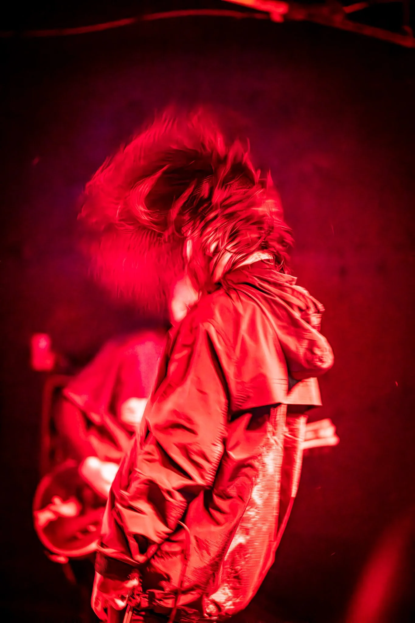Person wearing a red jacket and headphones, with their hair moving, illuminated by red lighting.