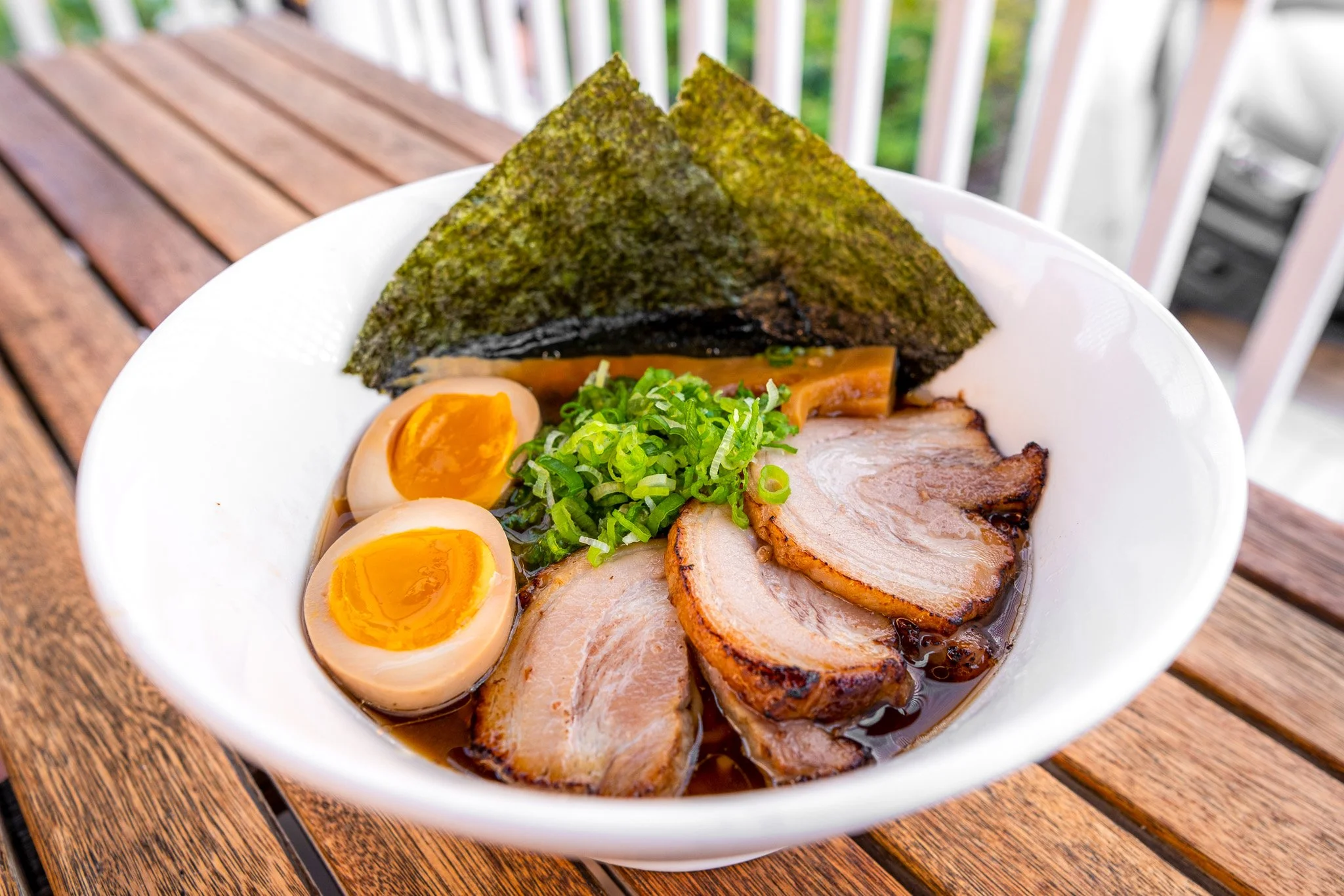 A bowl of ramen with sliced pork, soft-boiled eggs, green onions, seaweed, and bamboo shoots on a wooden table.