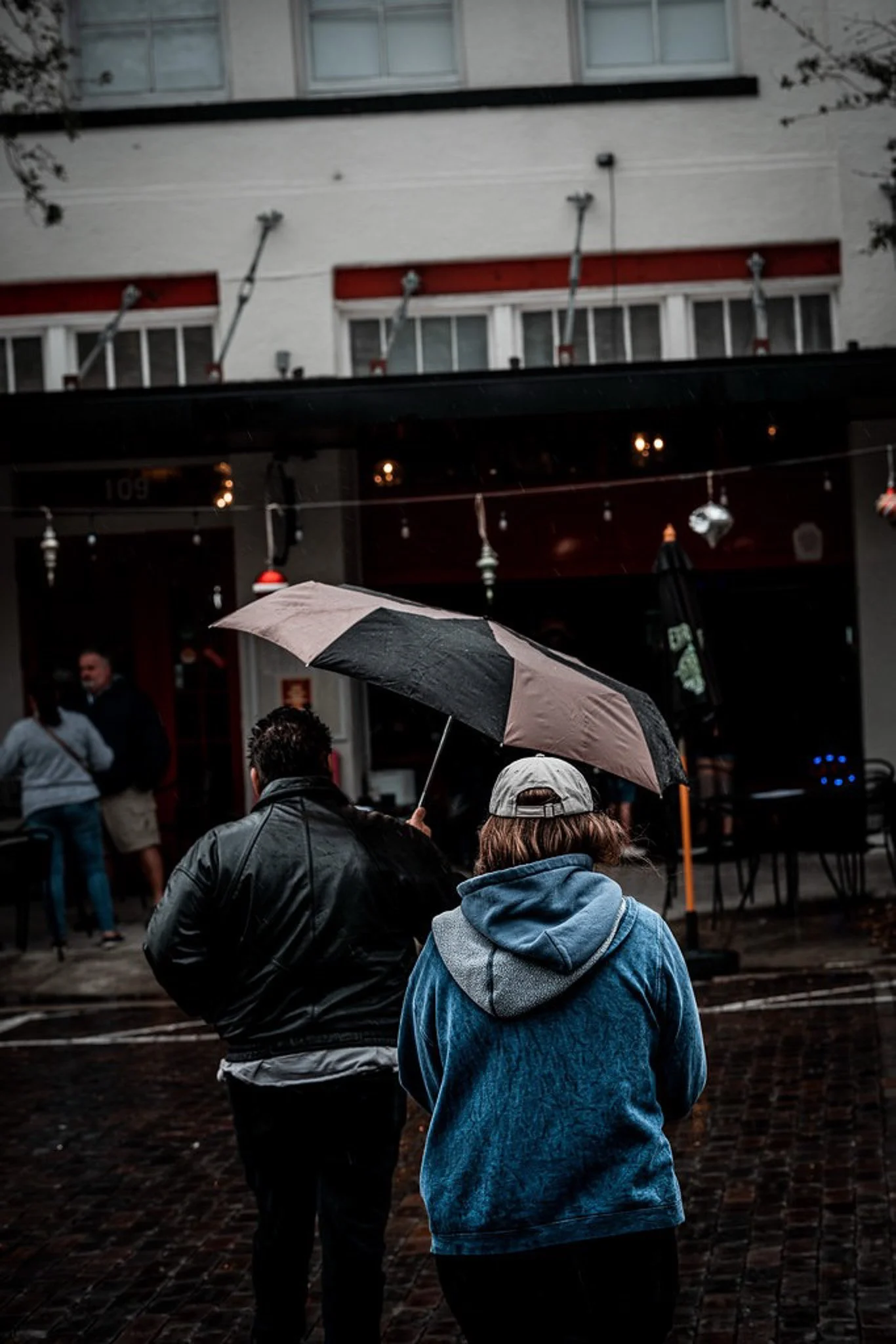 People walking on a rainy street with umbrellas outside a cafe or restaurant.