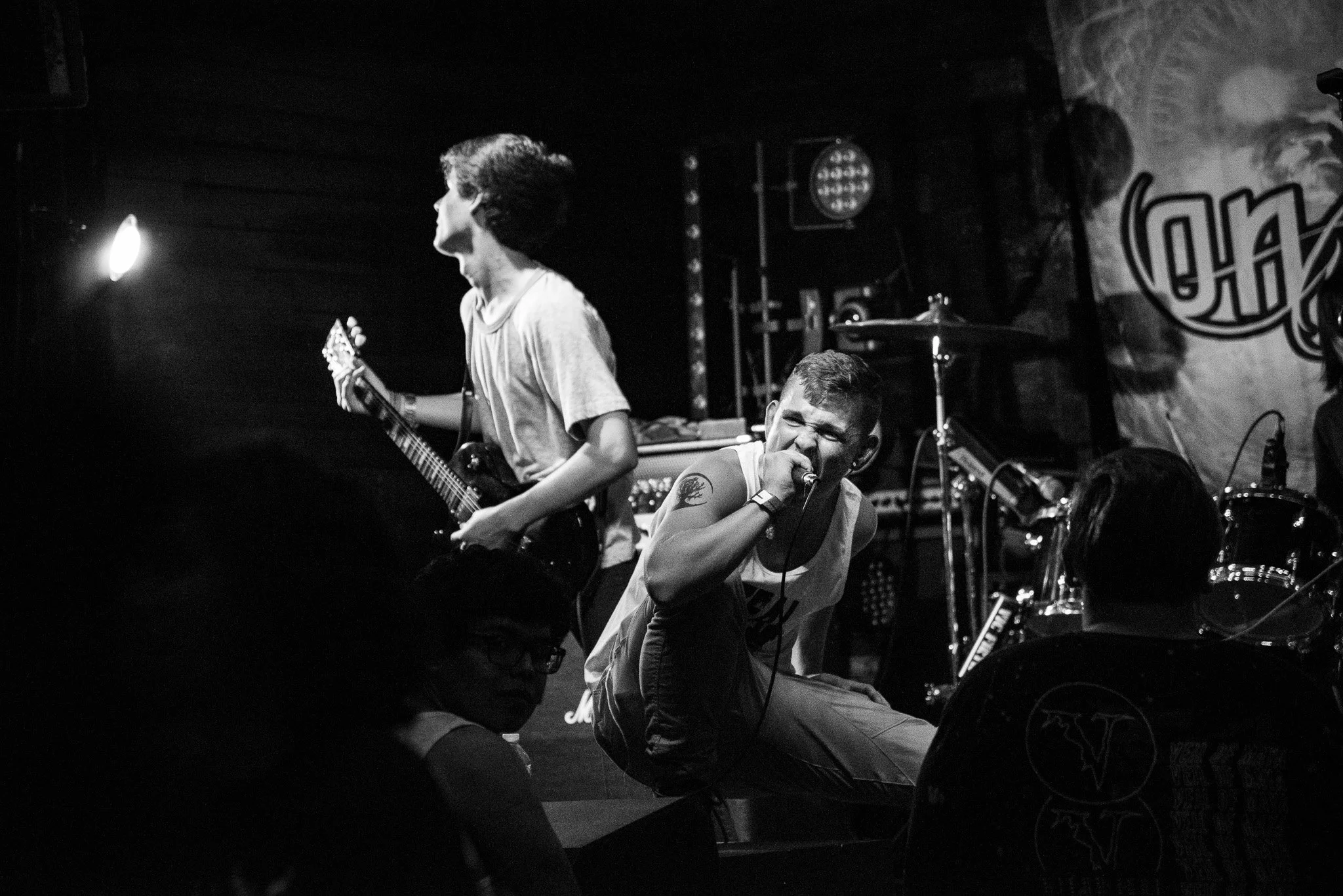 A band performing on stage, with a singer holding a microphone and a guitarist playing, in a dimly lit setting.