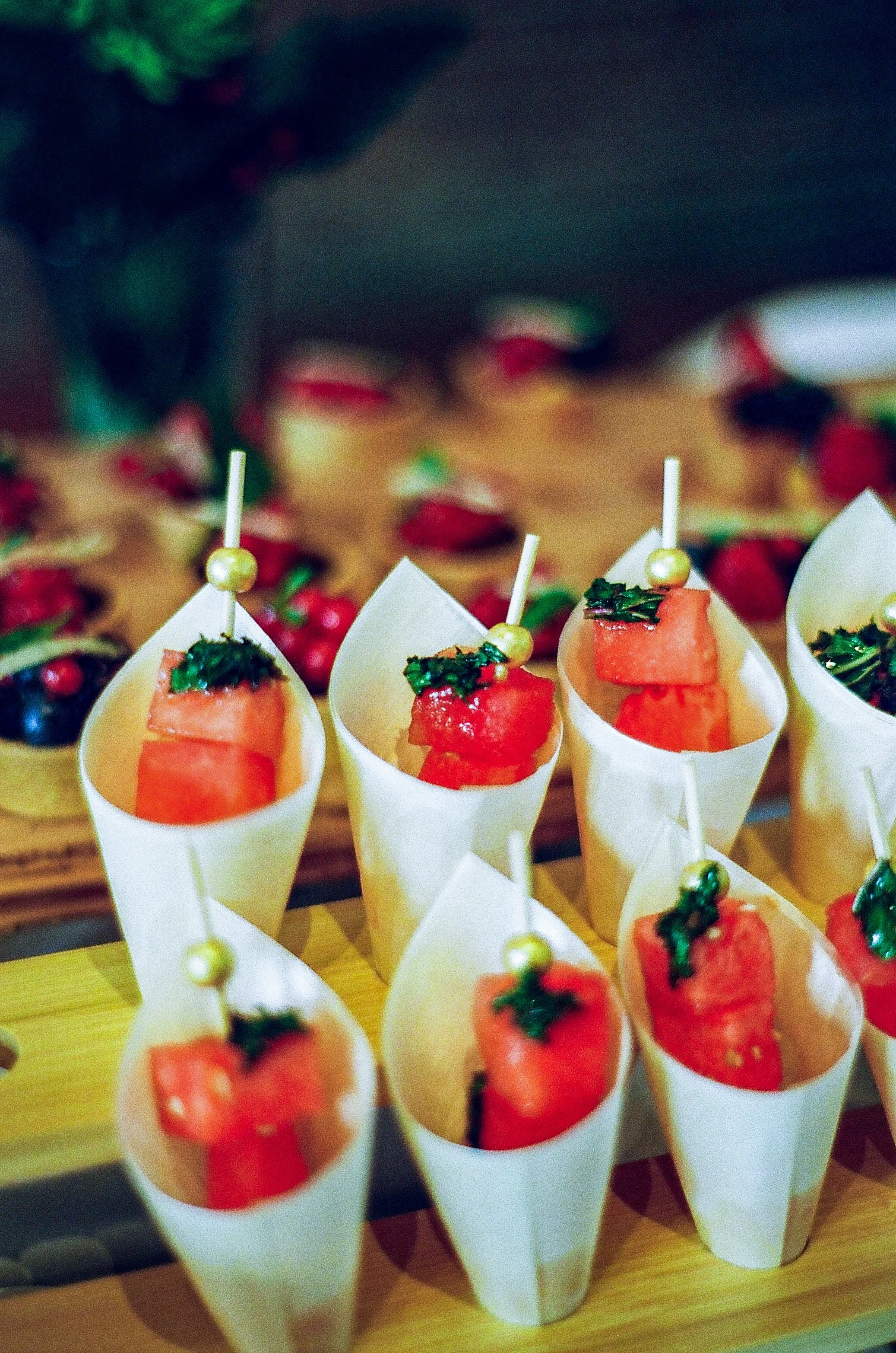 Mini appetizer cups filled with diced watermelon and garnished with chopped herbs, inserted with decorative toothpicks, served at a festive gathering.