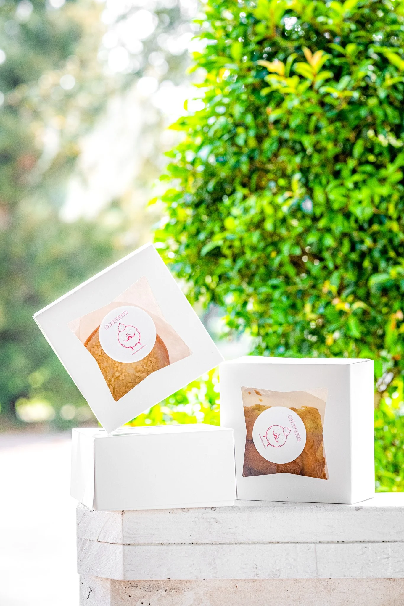 Three white boxes with cookies inside, labeled with a pink pig logo, are placed on a white surface outdoors with trees and greenery in the background.