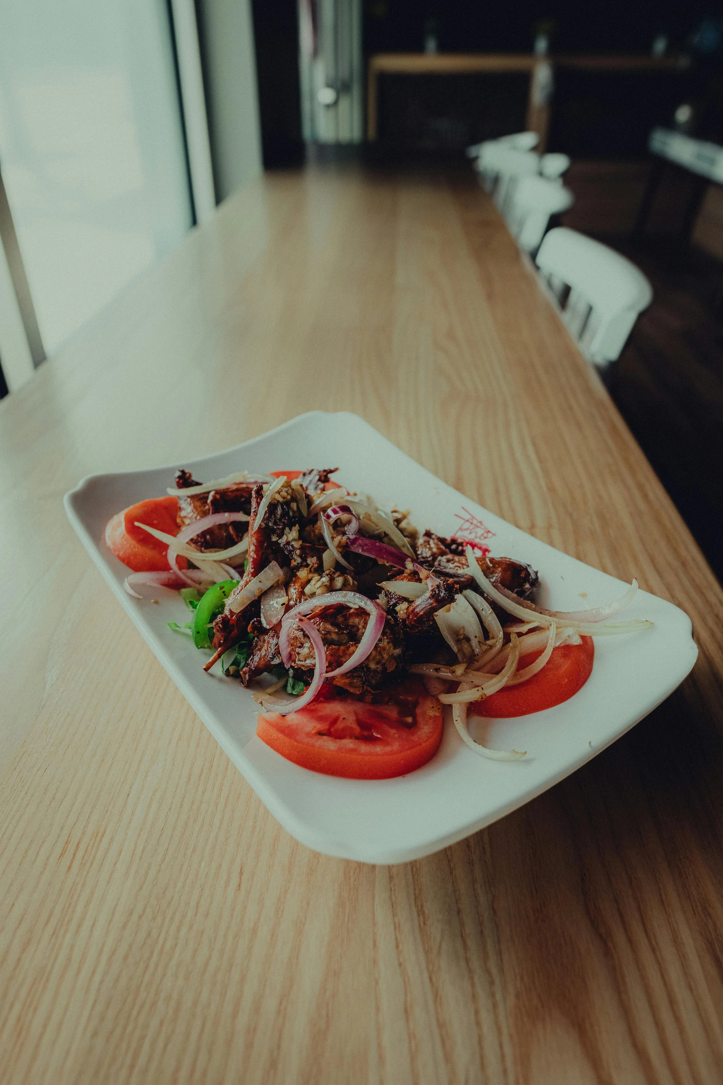 A plate of salad with sliced tomatoes, onions, and grilled meat on a wooden table at a restaurant.