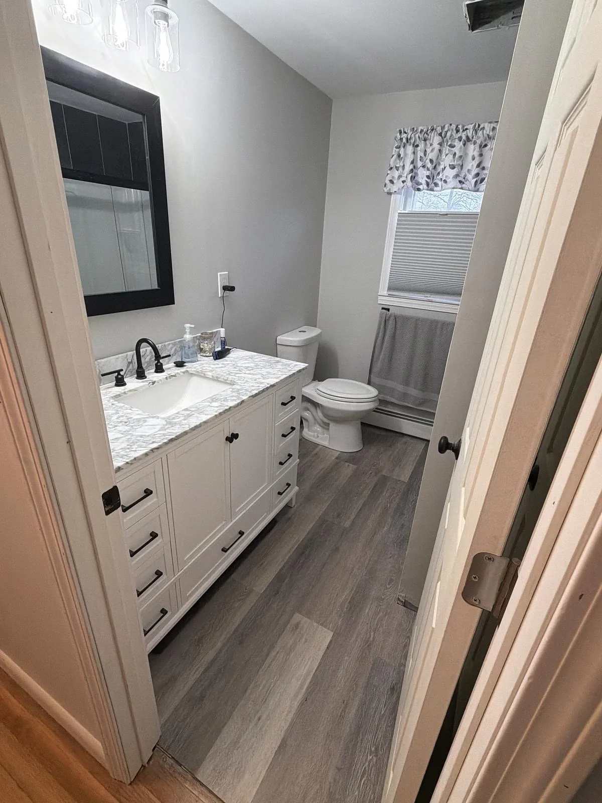 Finished bathroom remodel with marble-top vanity, new flooring and fixtures