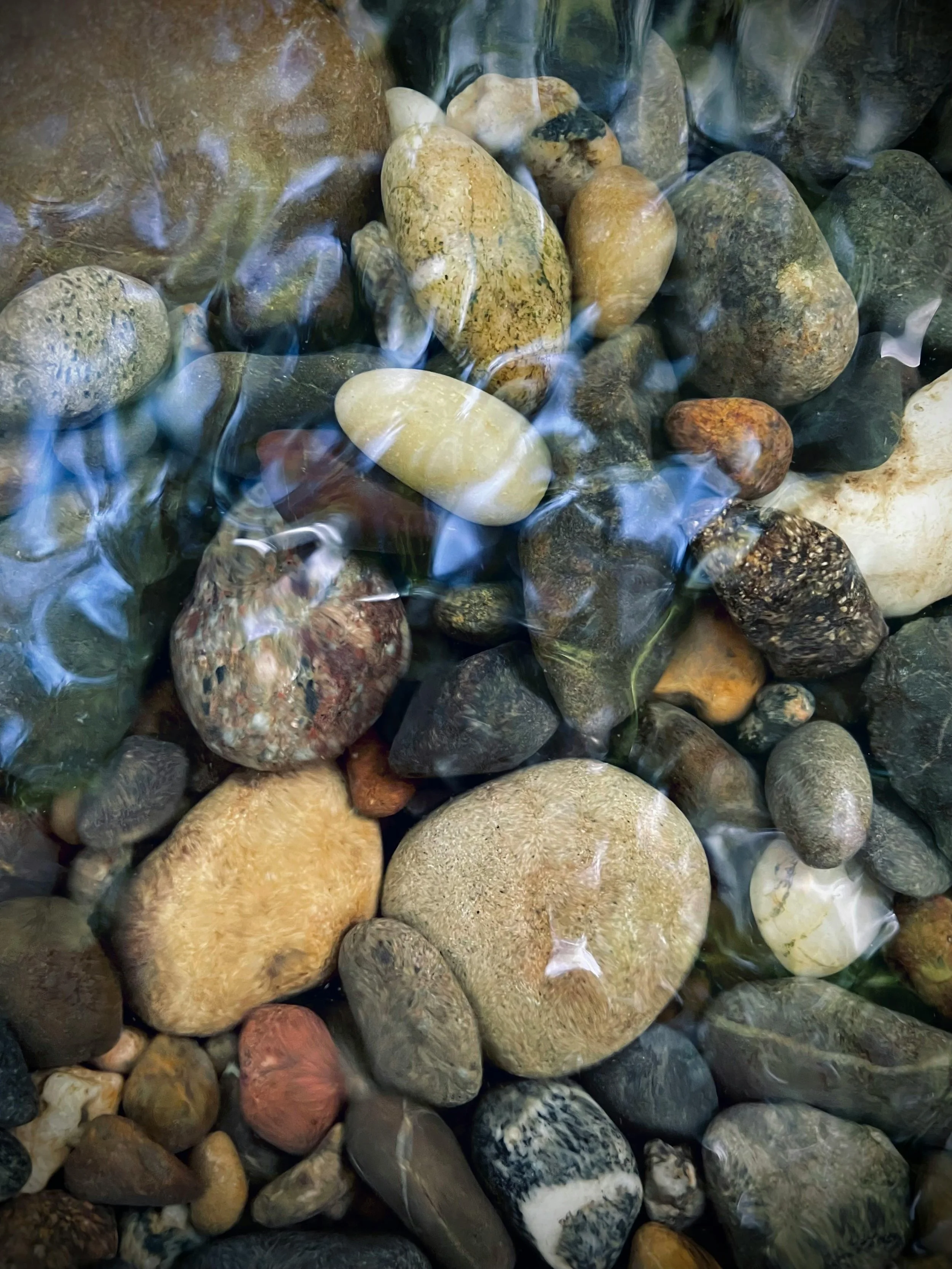 Close-up of multicolored smooth river stones beneath flowing water.