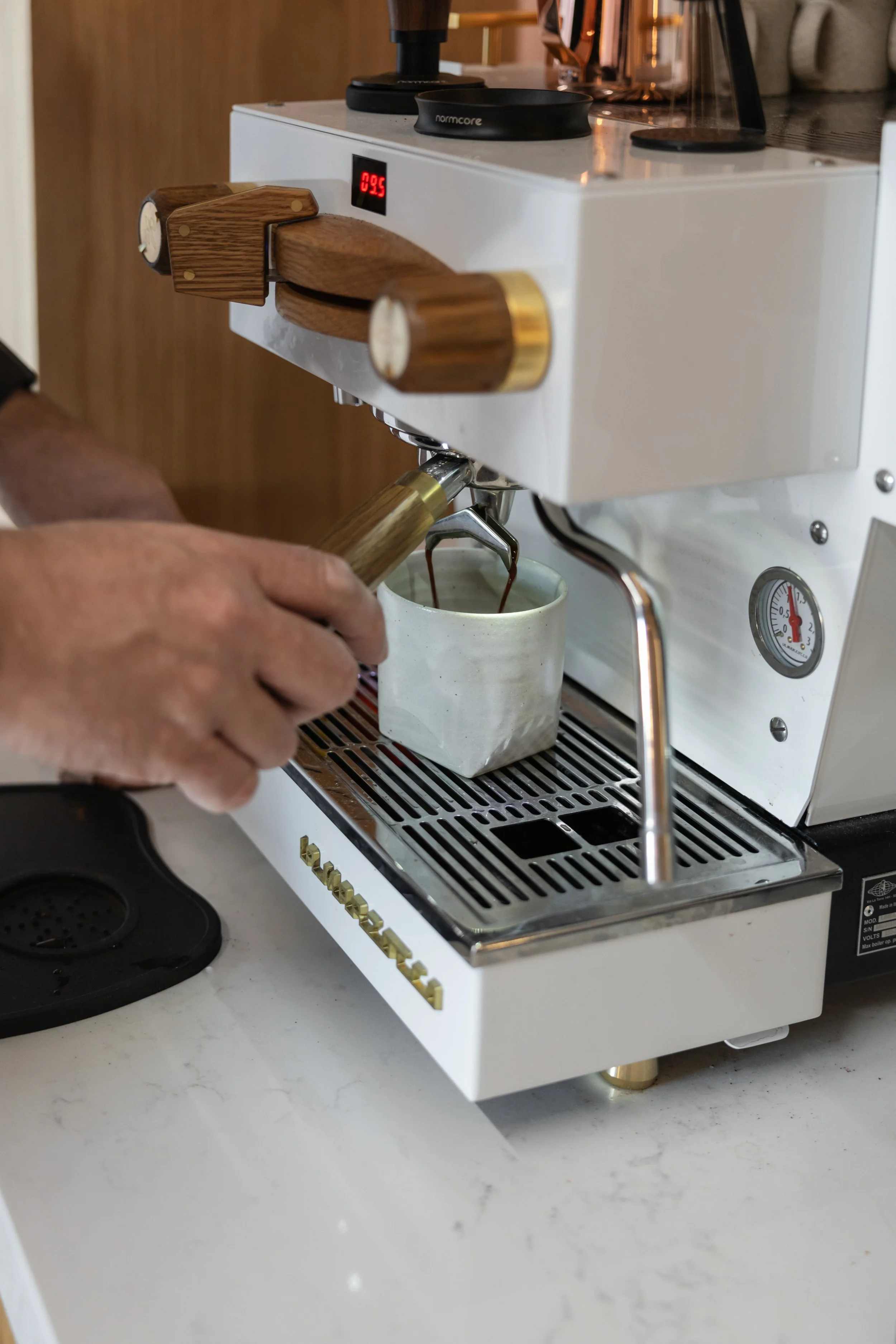 Person pulling espresso shot from a coffee machine into a ceramic cup.