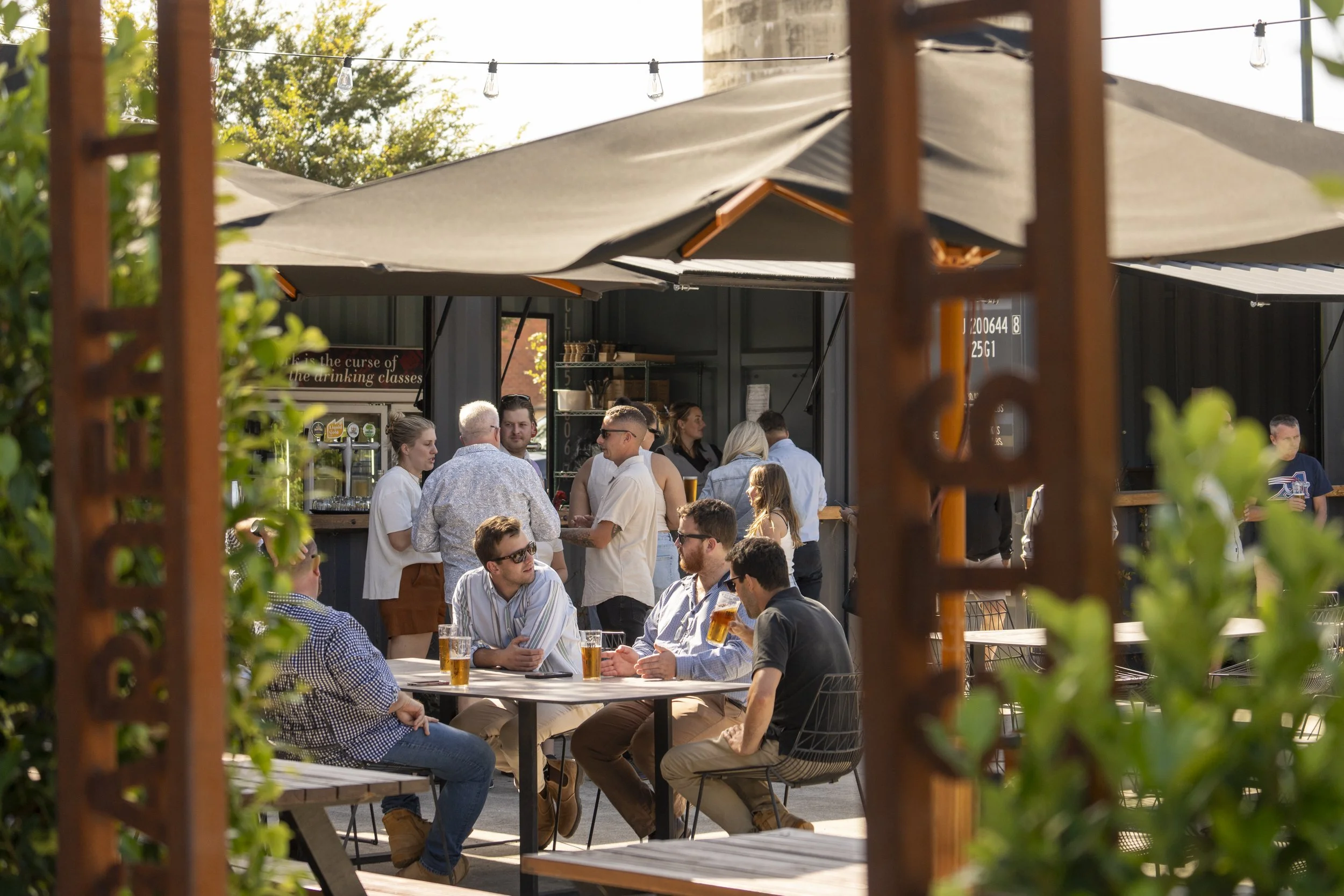 People enjoying drinks and socializing at an outdoor bar area with umbrellas and string lights.