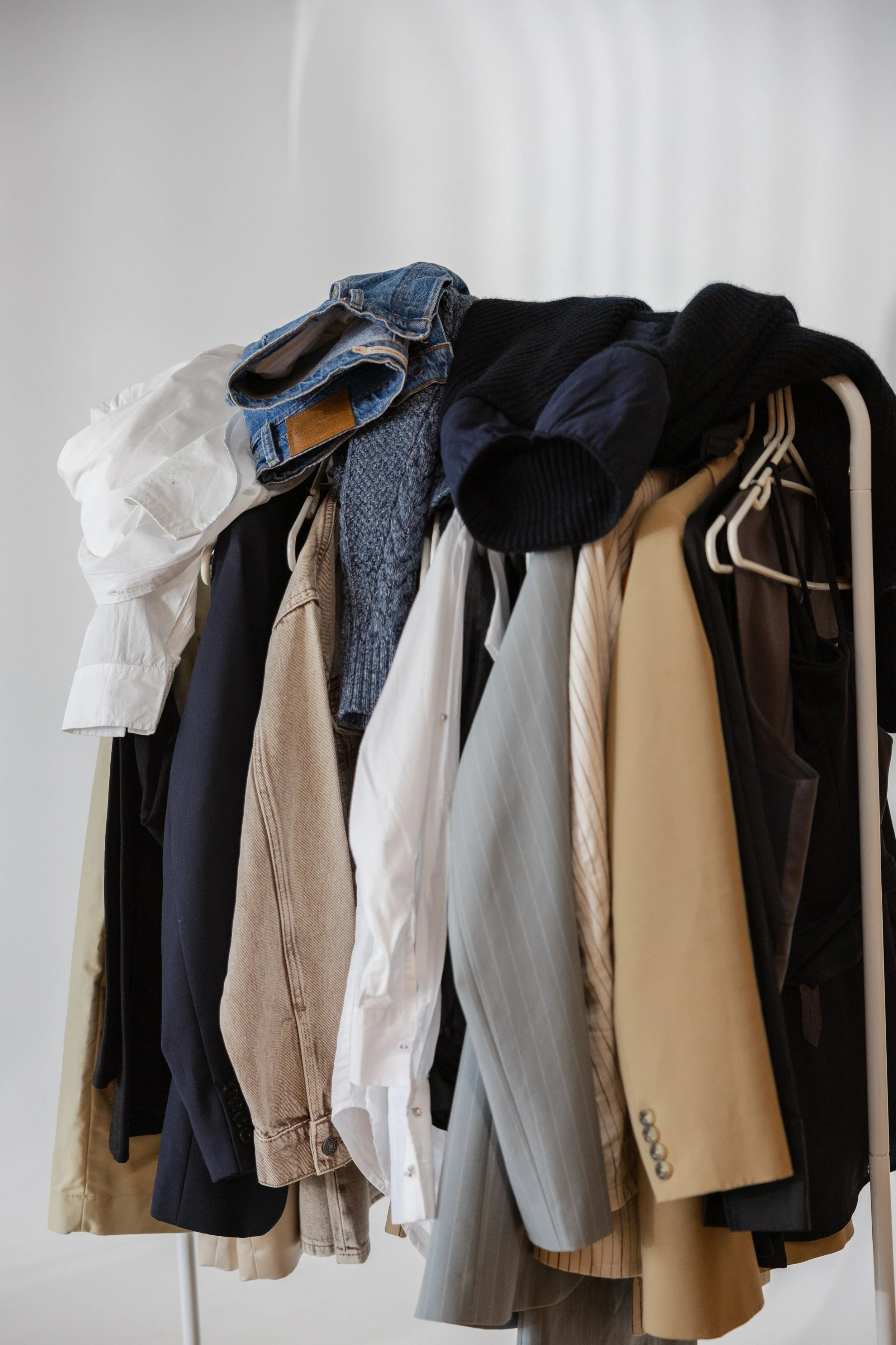Clothes on a white clothing rack, including jackets, shirts, pants, and a sweater.
