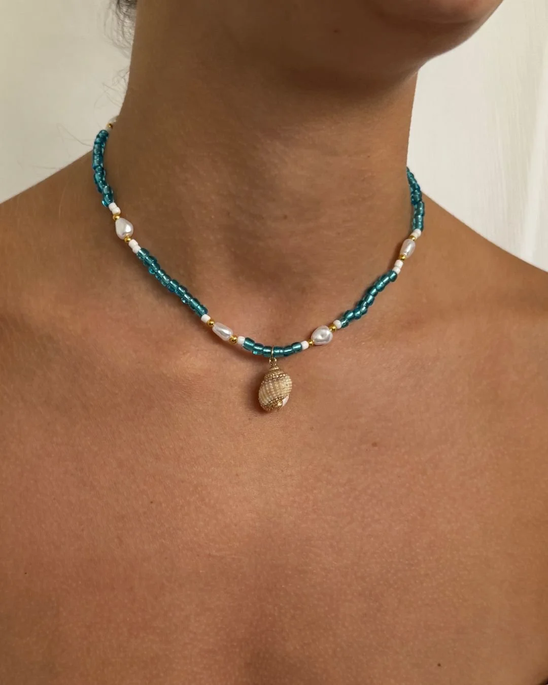 Beaded necklace with pearls and a shell pendant worn on a woman's neck.