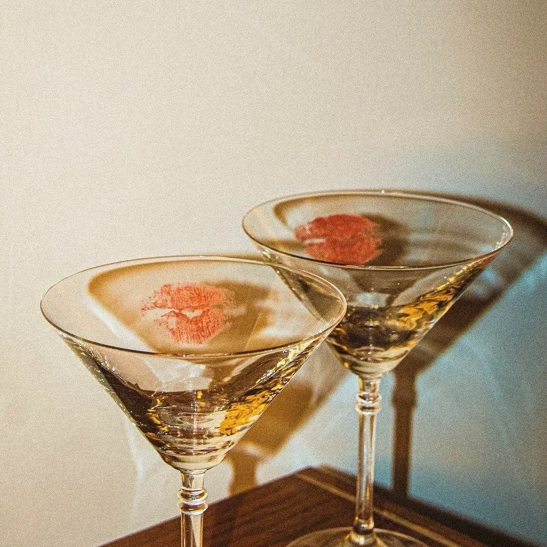 Two martini glasses with lips-shaped candy in the bottom of each glass, placed on a wooden surface, casting shadows on the background.