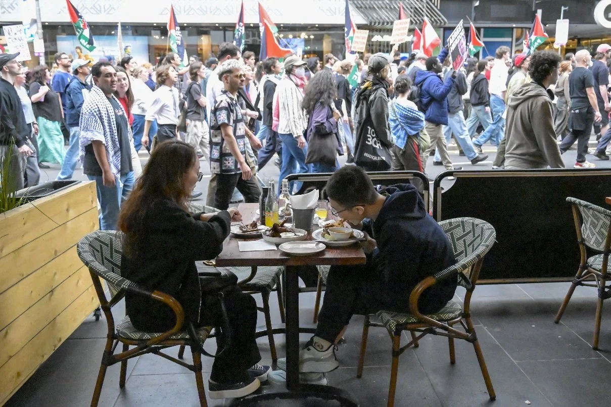 This documentary photograph was taken during a pro-Palestine march through Melbourne’s CBD, showing public protest, political symbolism, and everyday human moments within an urban demonstration. Photo by Farhad Rajabali