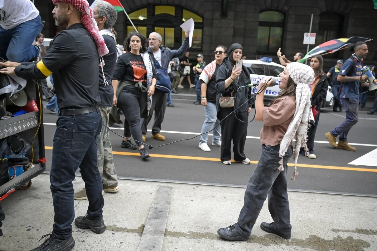 This documentary photograph was taken during a pro-Palestine march through Melbourne’s CBD, showing public protest, political symbolism, and everyday human moments within an urban demonstration. Photo by Farhad Rajabali