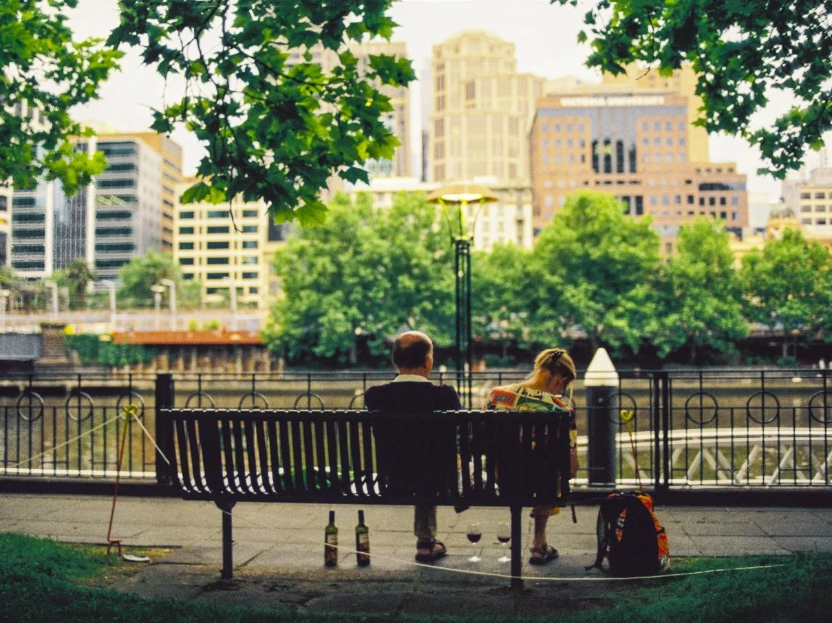 A quiet afternoon along the Yarra River in Melbourne, where two people sit side by side, sharing drinks against the backdrop of the city. Shot on 35mm film, this image captures a fleeting moment of everyday life, blending urban rhythm with human pres