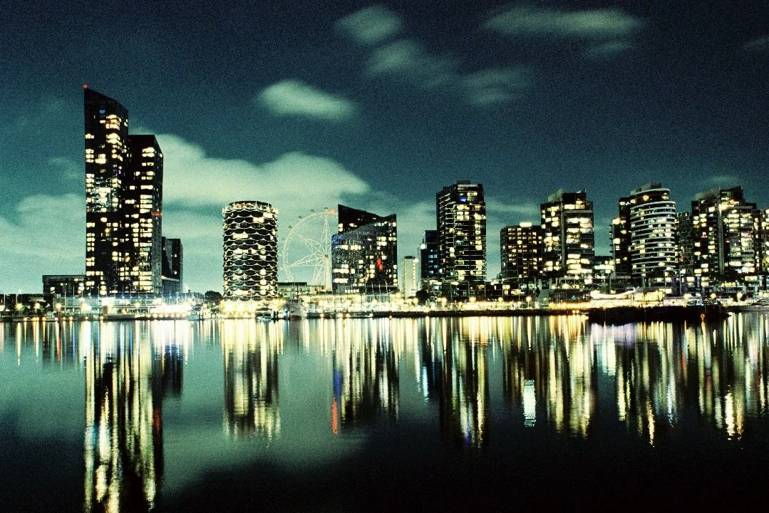 A quiet night at Melbourne Docklands, where illuminated towers stretch across the water and dissolve into soft reflections on the Yarra River. Captured on a Nikon FM 35mm film camera, this photograph documents the stillness of the city after hours — 