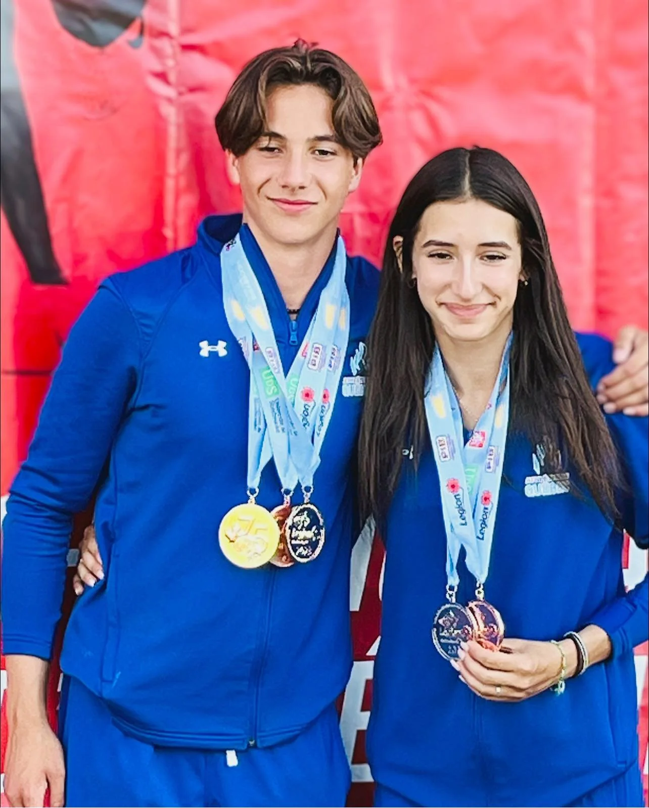 Deux jeunes athlètes portent des médailles de compétition et posent pour une photo, vêtus de survêtements bleus.