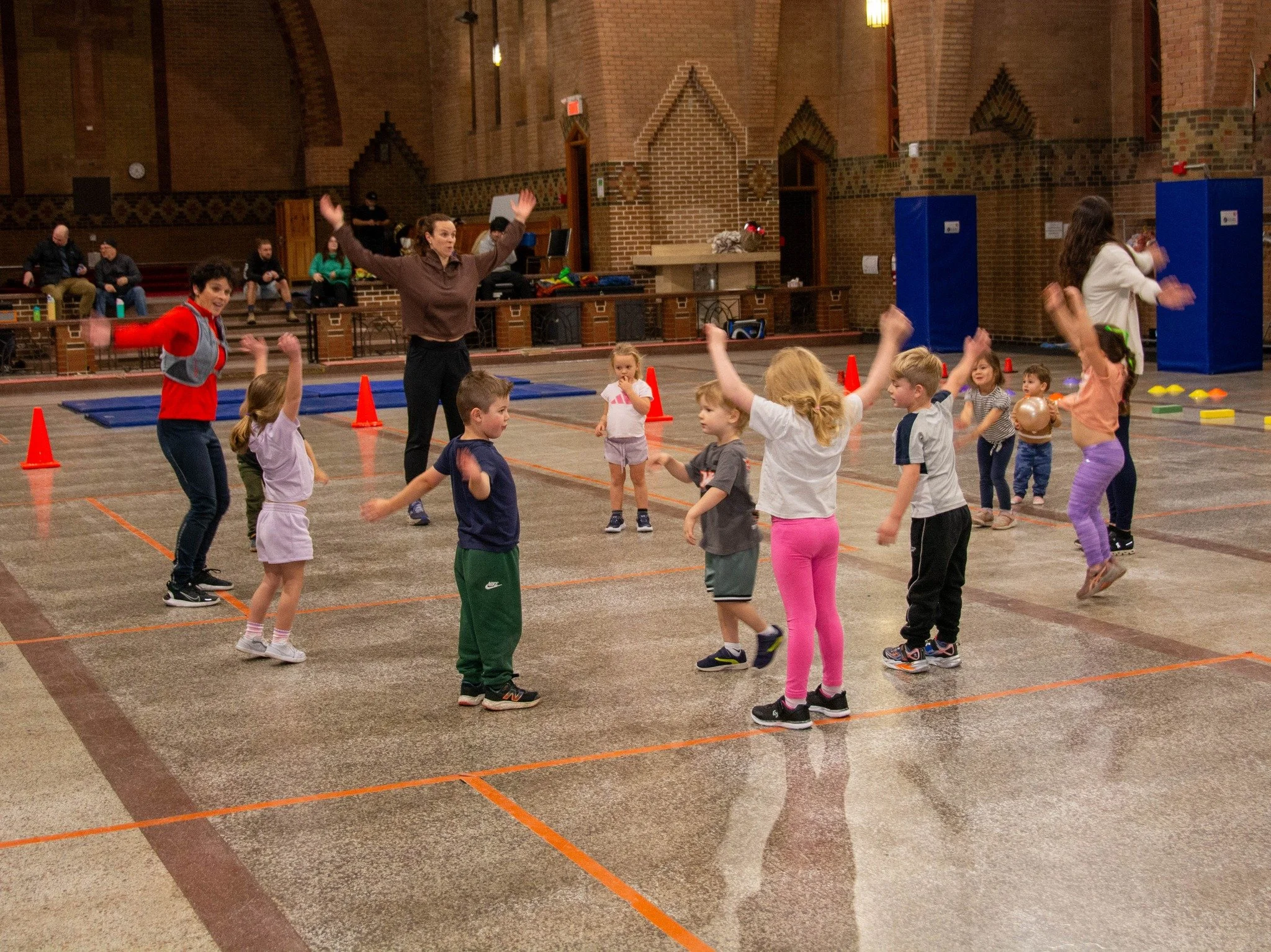 Groupe d'enfants et deux adultes en train de jouer ou danser dans une salle de sport ou gymnase.