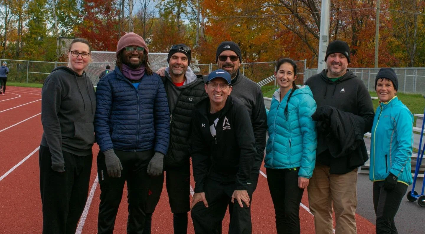 Groupe de huit personnes en vêtements de sport, posant pour une photo sur une piste de course en extérieur, à l'automne.
