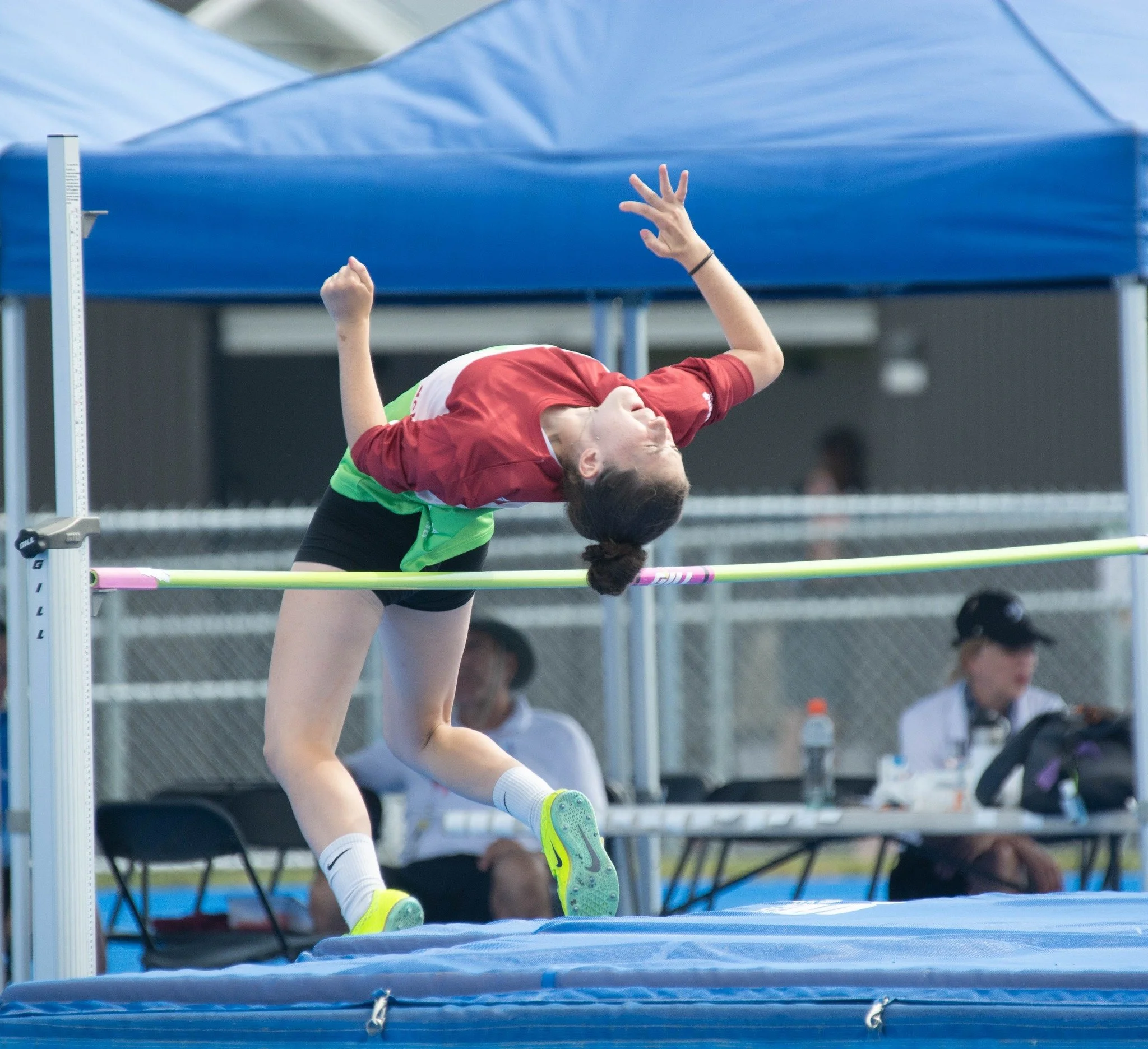 Une femme en pleine tentative de saut en hauteur lors d'une compétition sportive, en train d'atteindre la barre de saut.