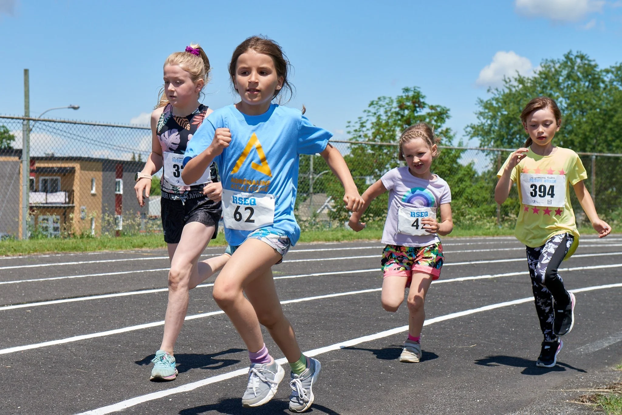Jeunes filles en course sur une piste d'athlétisme en plein air par une journée ensoleillée.