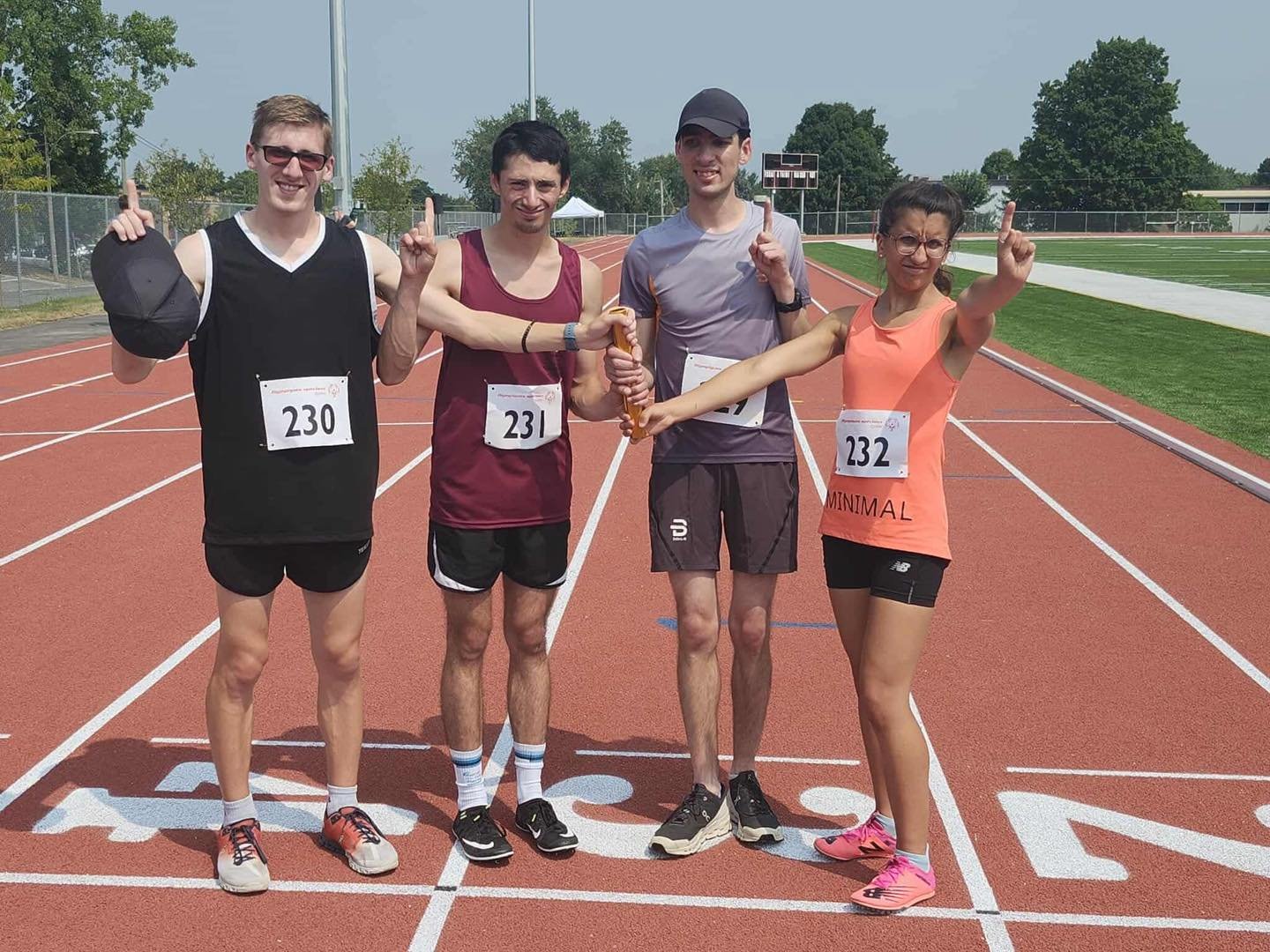 Quatre coureurs posant sur une piste d'athlétisme, souriants et pointant vers le ciel.