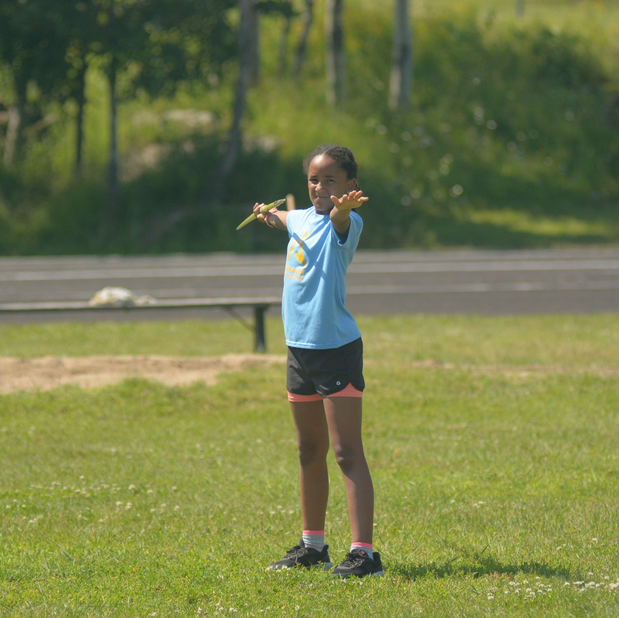 Une jeune fille en tenue de sport, tenant un javelot, semble s'apprêter à lancer un javelot.