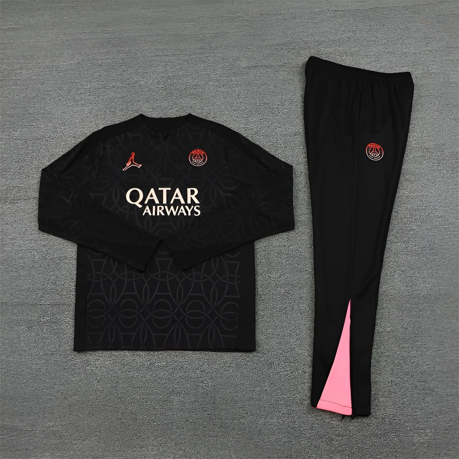 Black soccer jersey with sponsor logo 'Qatar Airways' and red Paris Saint-Germain crest, paired with black and pink athletic pants, laid out on gray carpet.