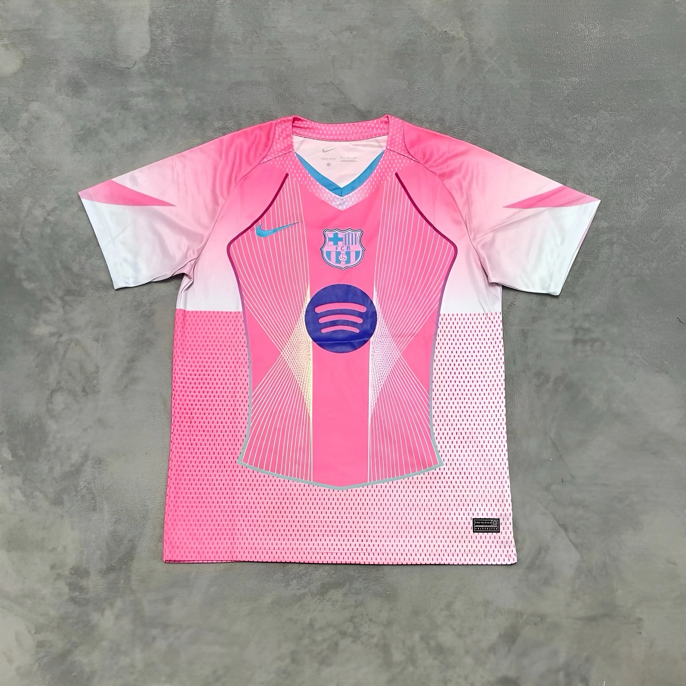 Pink and white FC Barcelona soccer jersey with sponsor logo and team crest on the front, laid flat on a gray concrete surface.