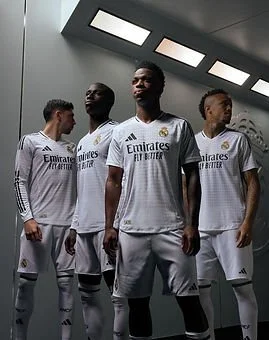 Four soccer players in white jerseys and shorts standing in a modern locker room with artificial lighting.