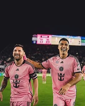 Two soccer players in pink jerseys celebrating on the field, smiling and appearing happy.