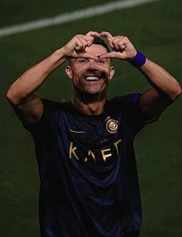 A man on a soccer field making a heart shape with his hands over his eyes.