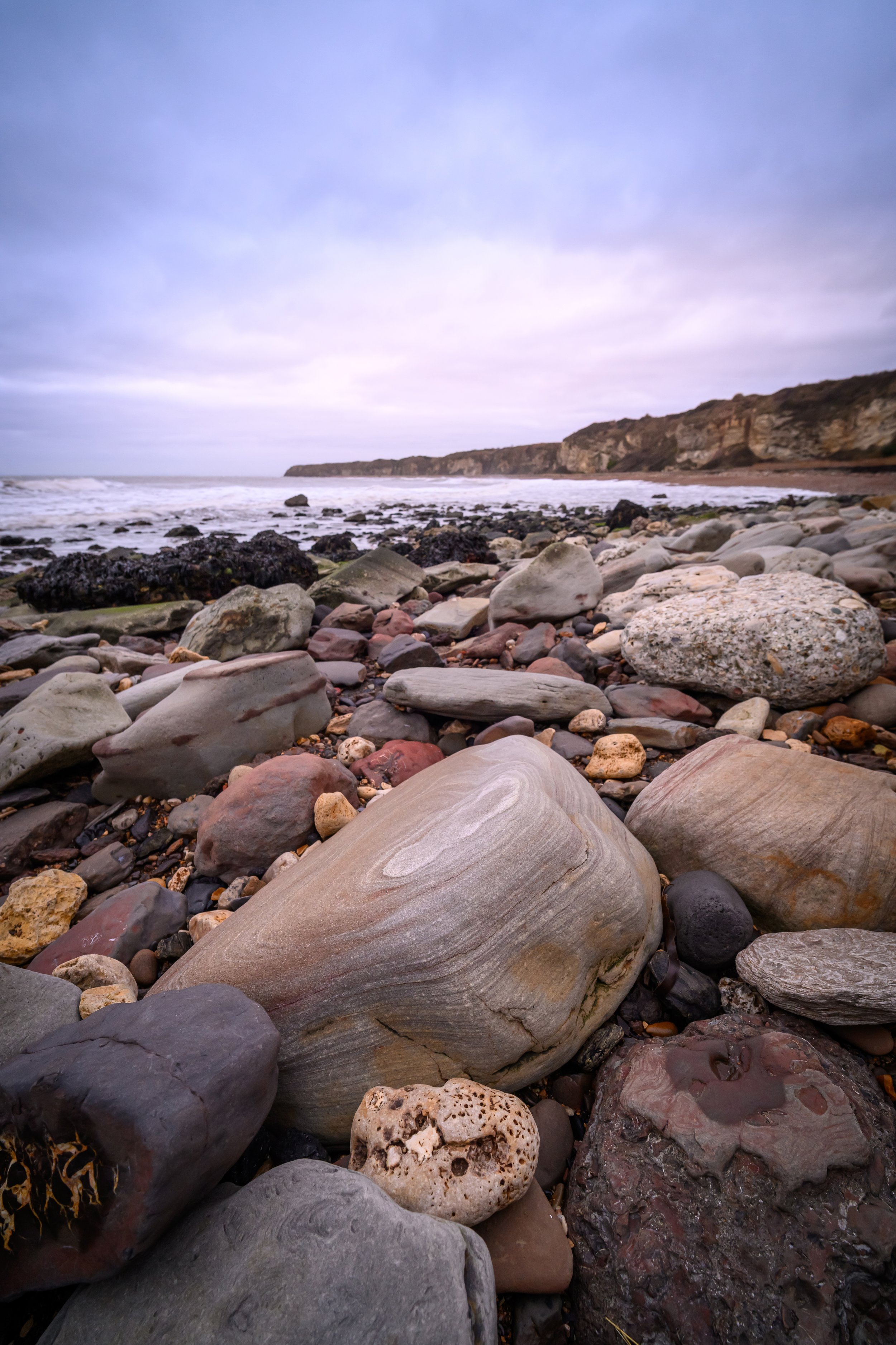 Rocky beach with ocean waves and cliffs under a cloudy sky.