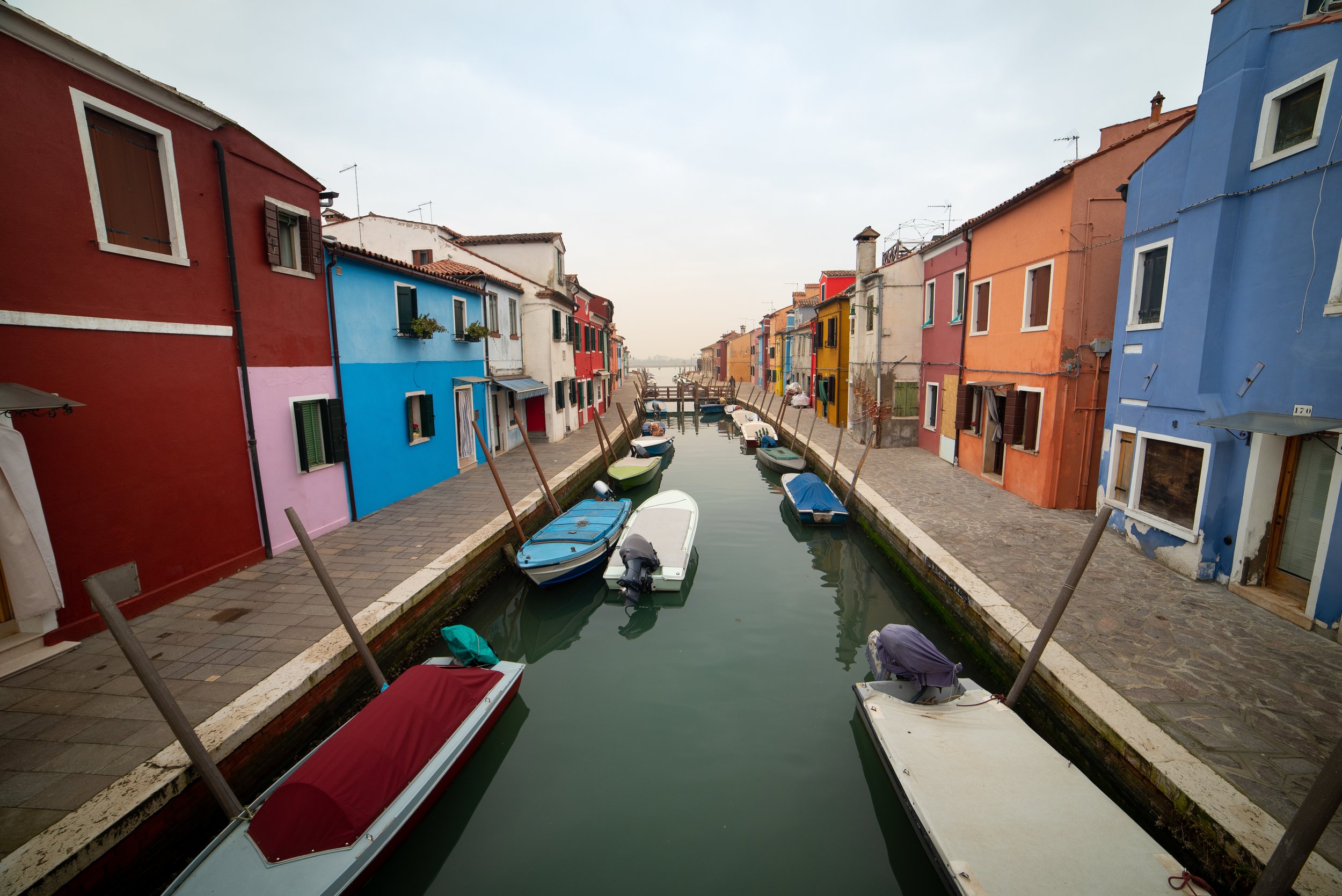 Colorful houses line a canal with several small boats docked along the water in a quaint village.