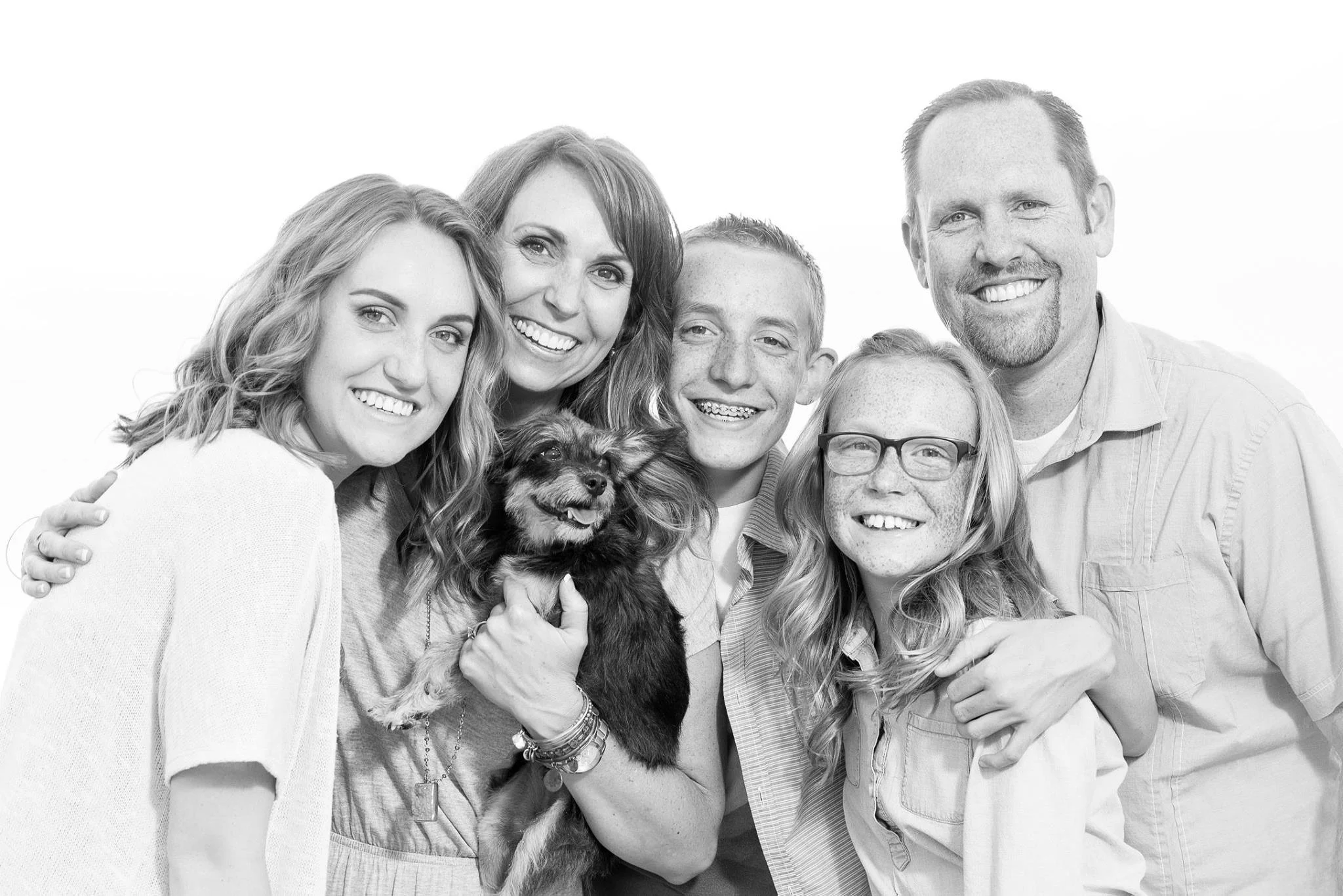 A happy multi-generational family group photo with five adults, one child, and a dog, all smiling and close together.