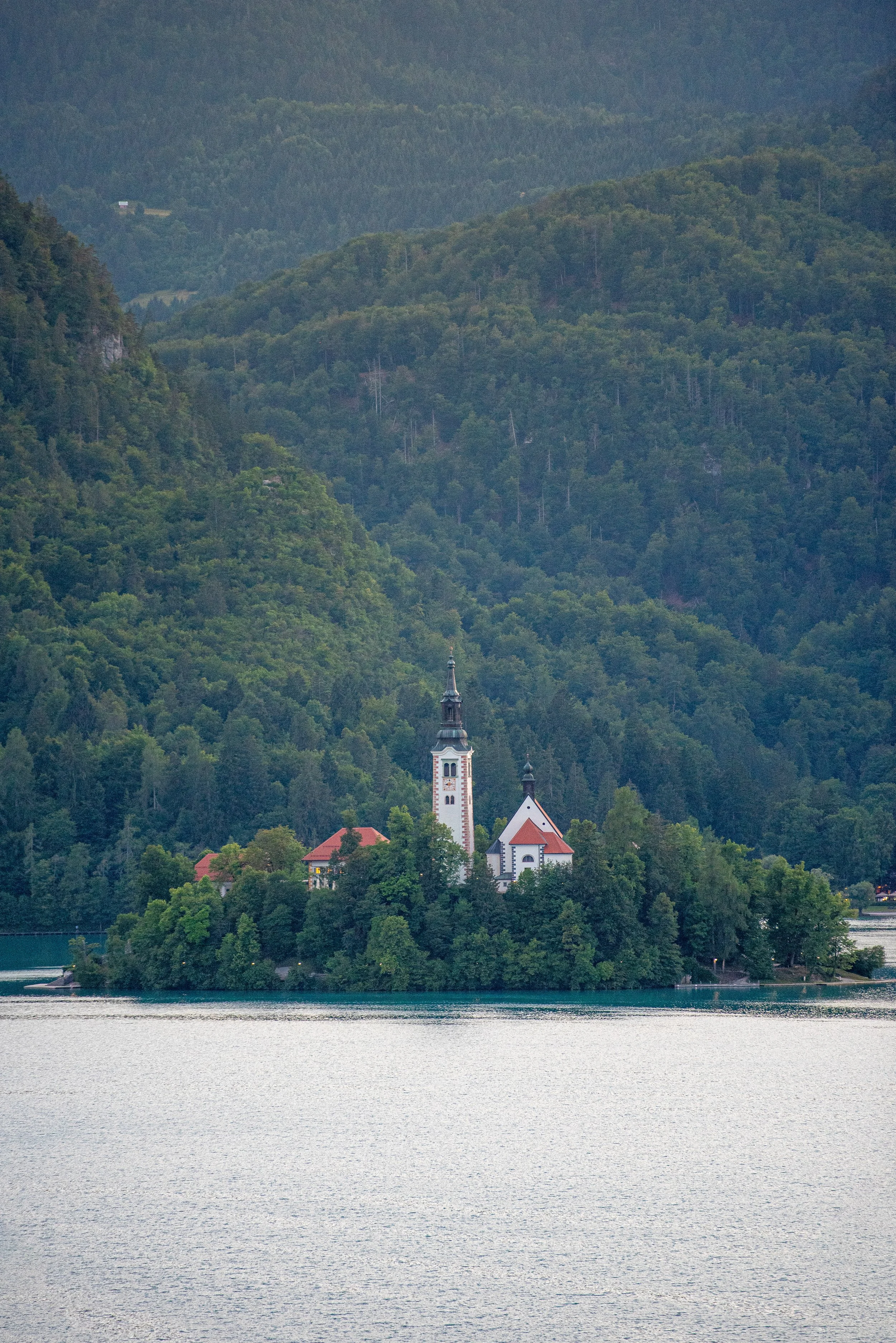 A church on a small island surrounded by water, with forested hills in the background.