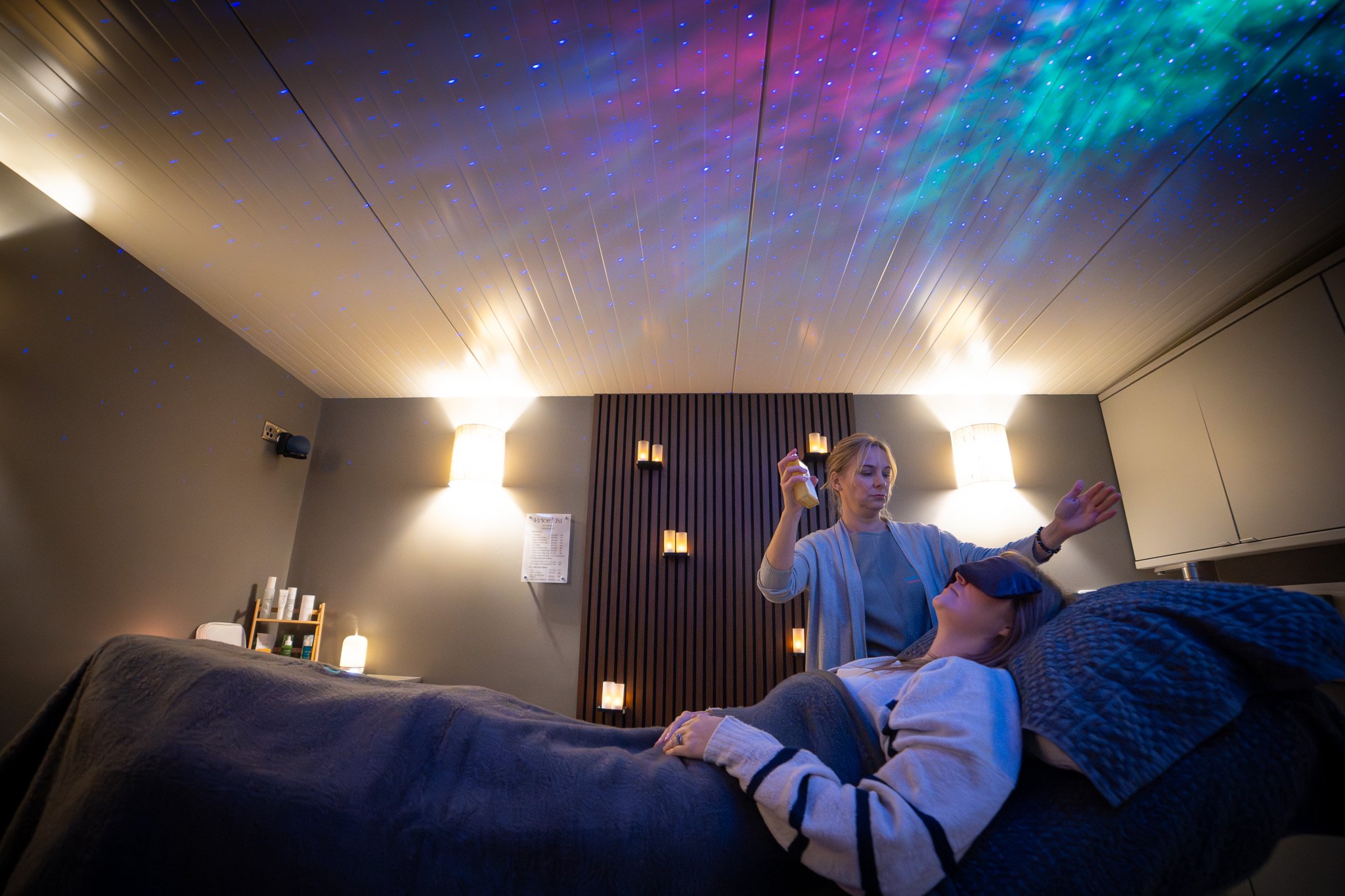 Woman receiving a spa or massage treatment while lying on her back in a dimly lit room with star projector lights on the ceiling.