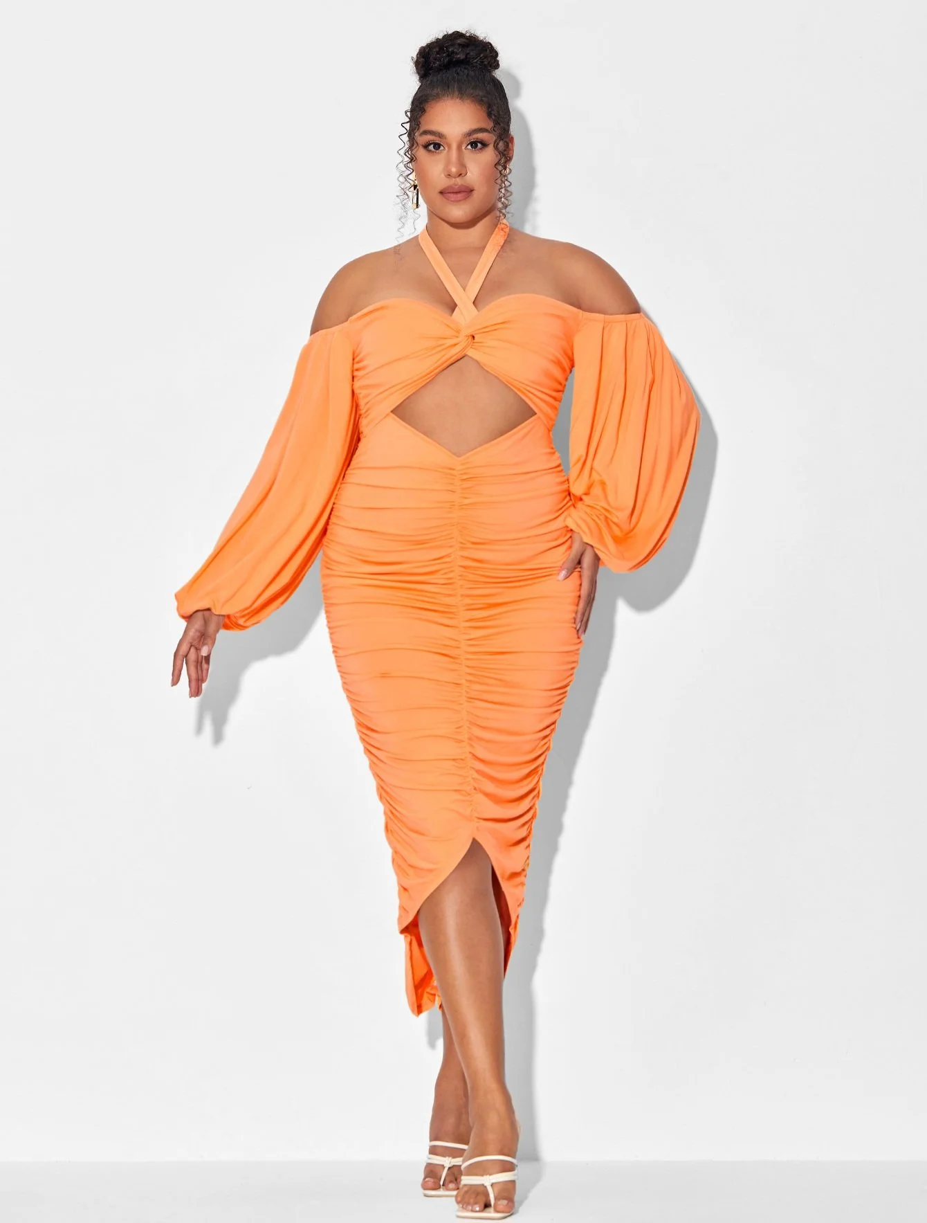 Woman in bright orange dress with puffed long sleeves, cutouts at midriff and hem slit, standing against white background.