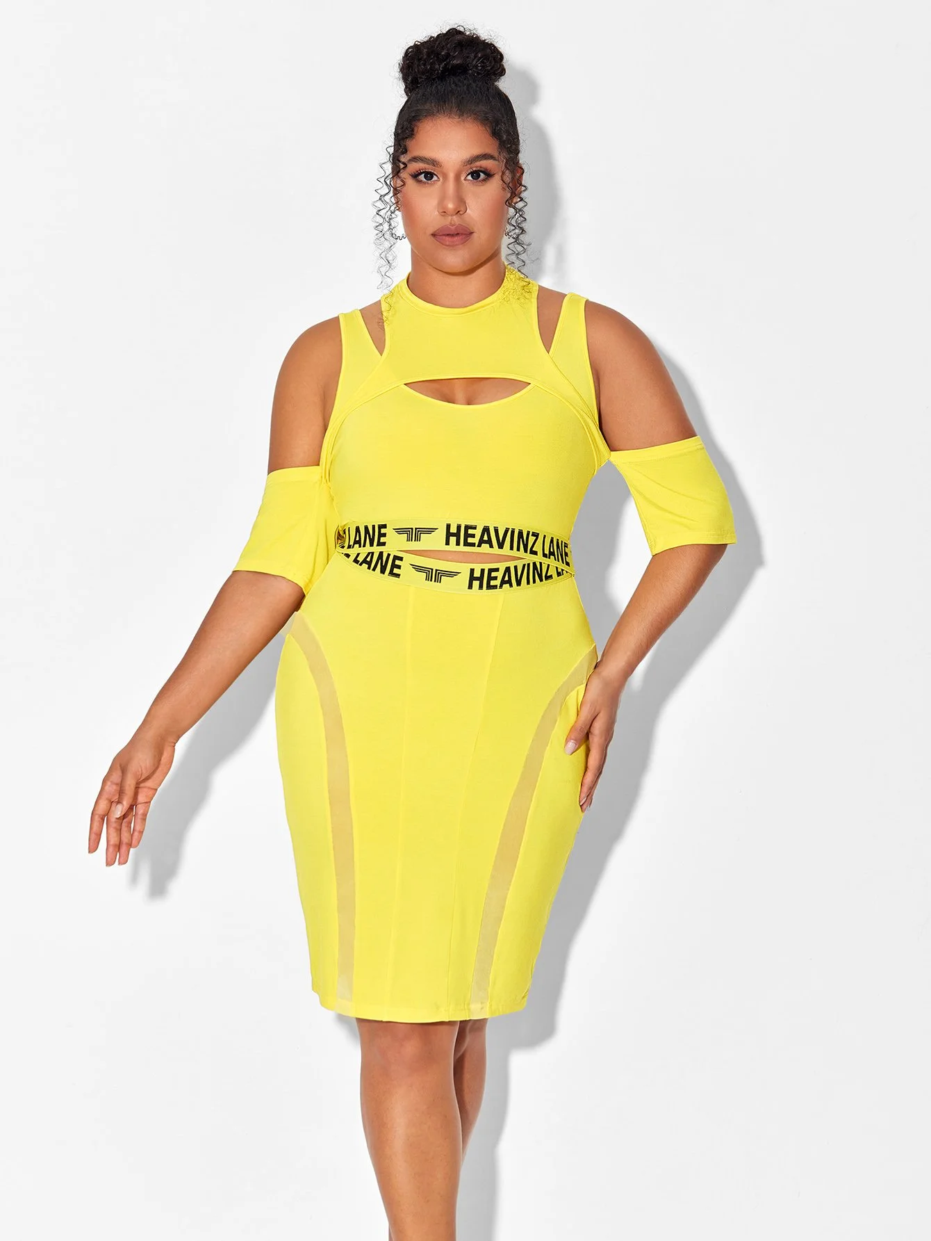 A woman wearing a bright yellow dress with cutouts, cold-shoulder sleeves, and black waistbands that say 'HEAVINZ' and 'LANE' in bold letters.