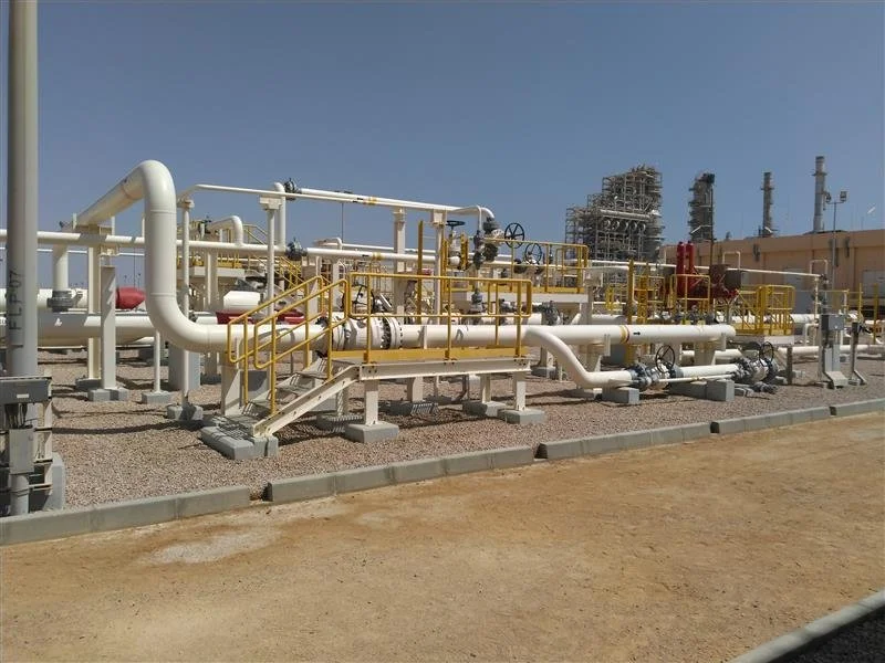 Industrial facility with pipelines, valves, and machinery under a clear sky.