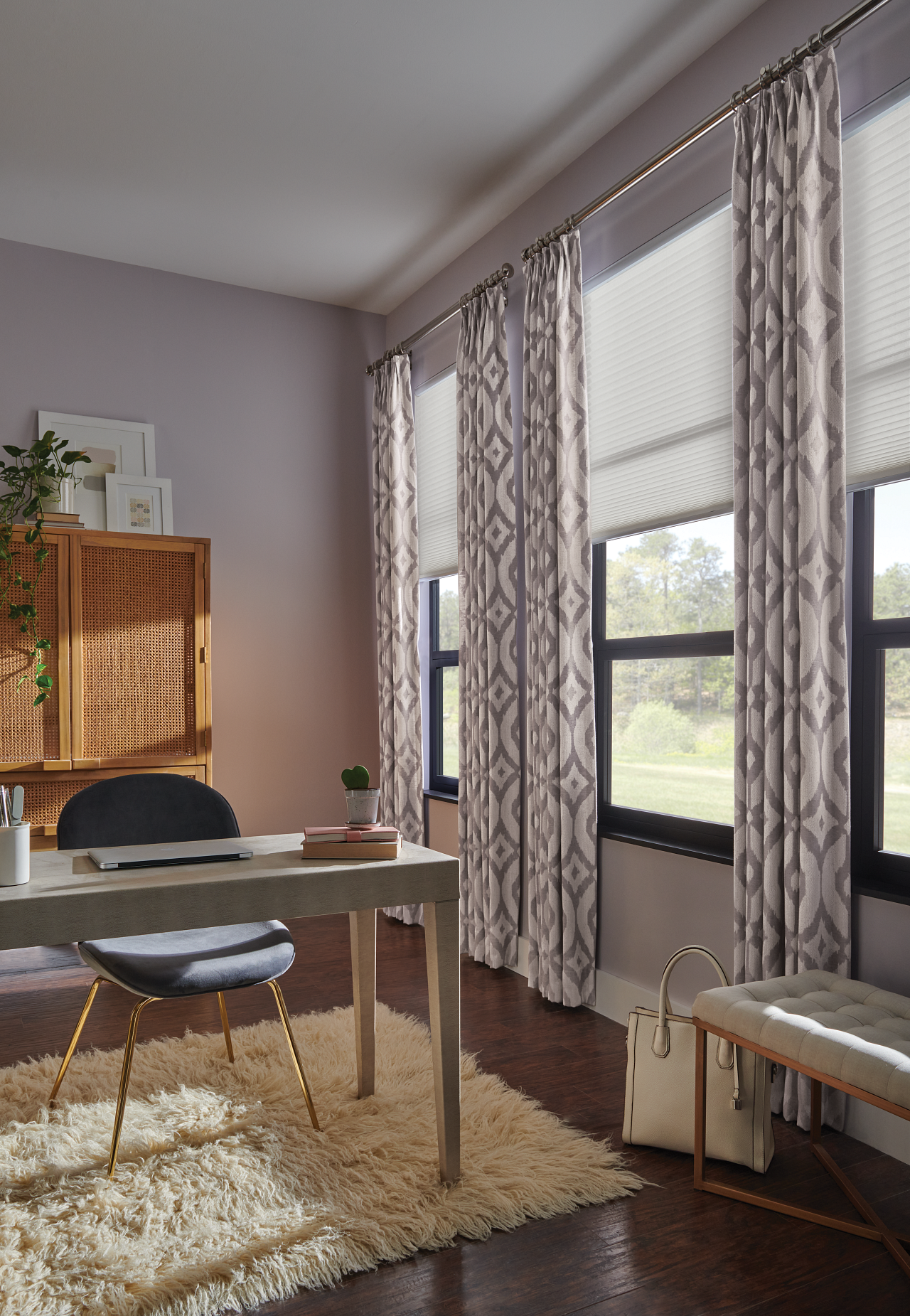 Interior of a room with a desk, a black chair, a cream-colored plush rug, a window with patterned curtains, a wooden cabinet, some framed artwork, a potted plant, and a white handbag.