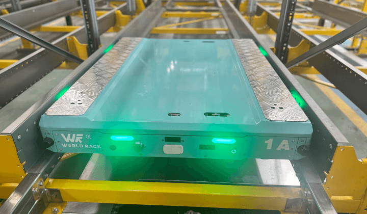 A green pallet shuttle with flashing lights is moving in a shuttle system.