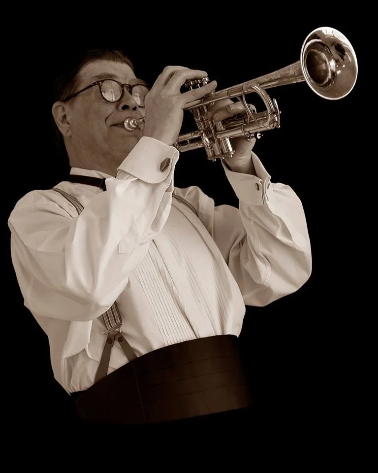 Man dressed in vintage formal attire playing a trumpet against a black background.