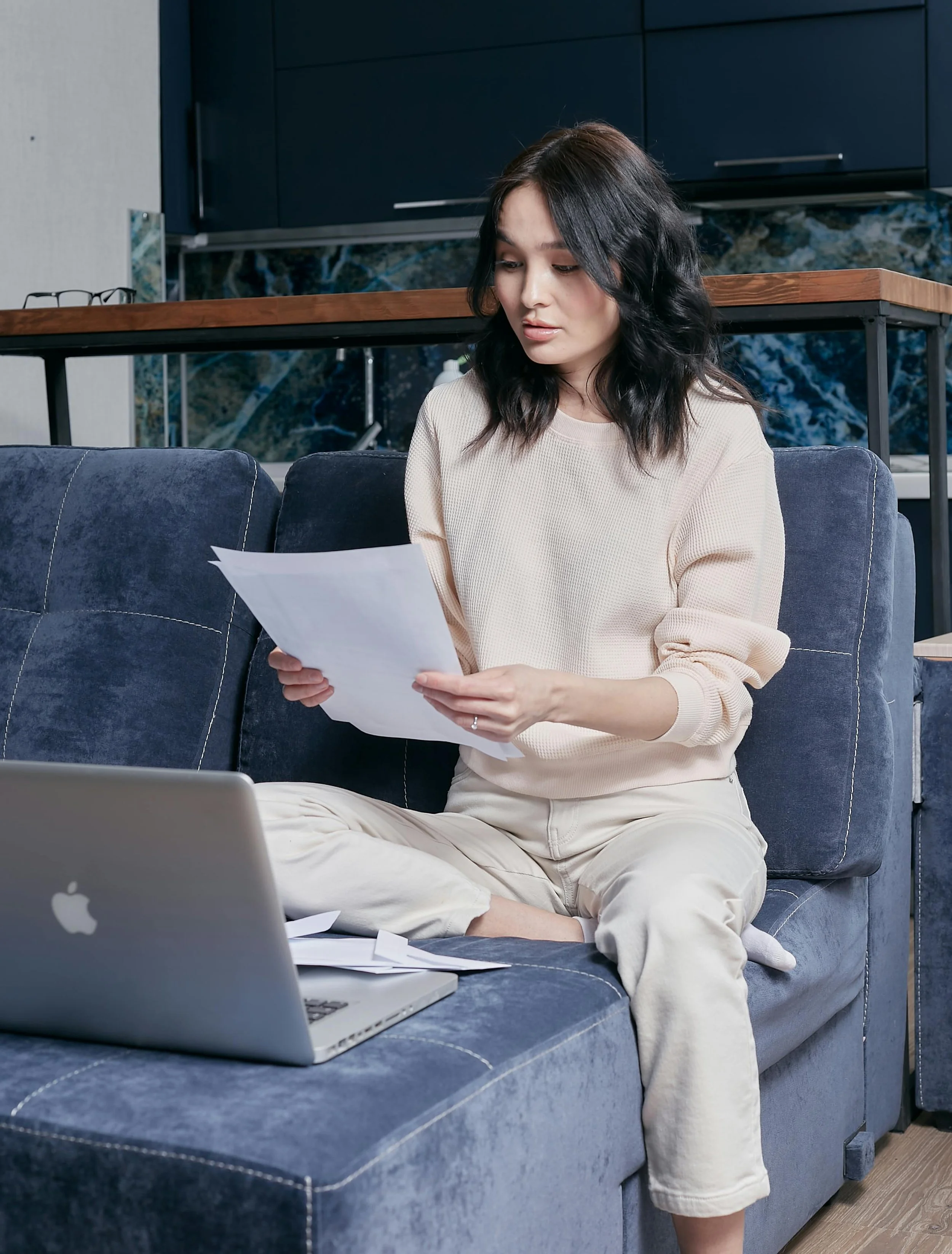 Woman in a cream sweater sitting on a sofa looking at papers with a worried expression, anxiety therapy in NYC