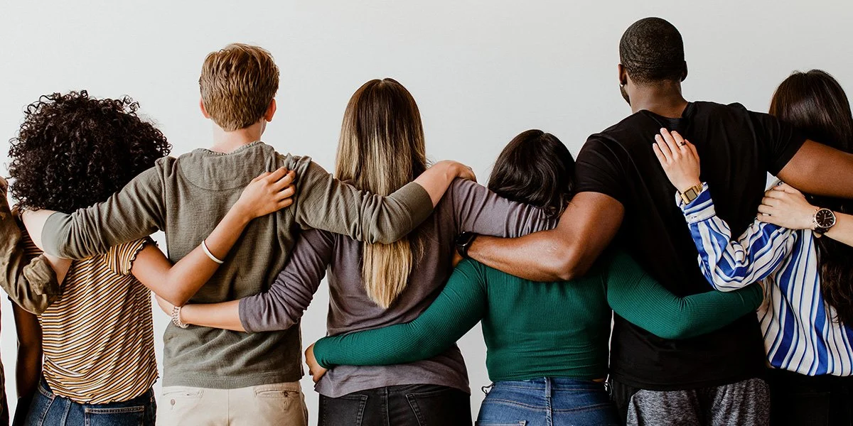 Group of diverse people standing with arms around each other, back view.