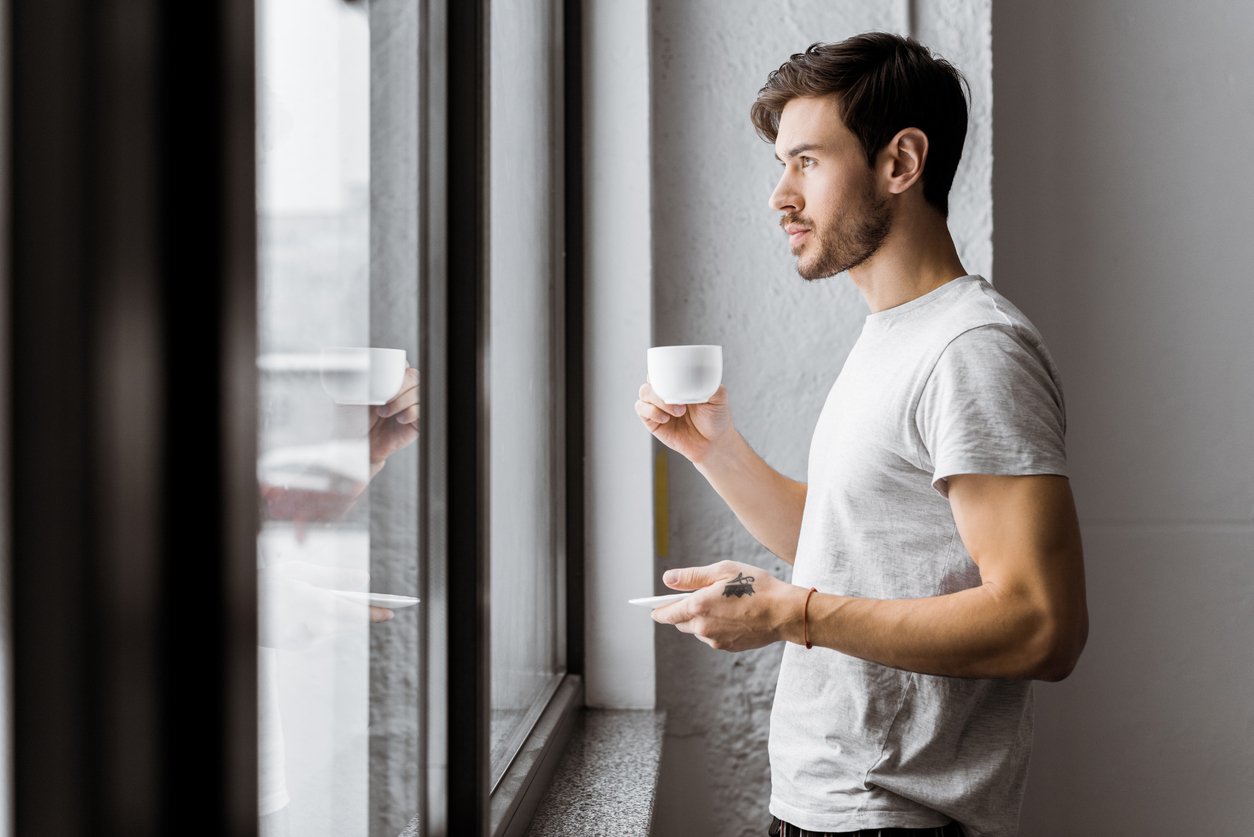 Man pausing by a window with coffee in a sunlit apartment, OCD therapy in New Jersey